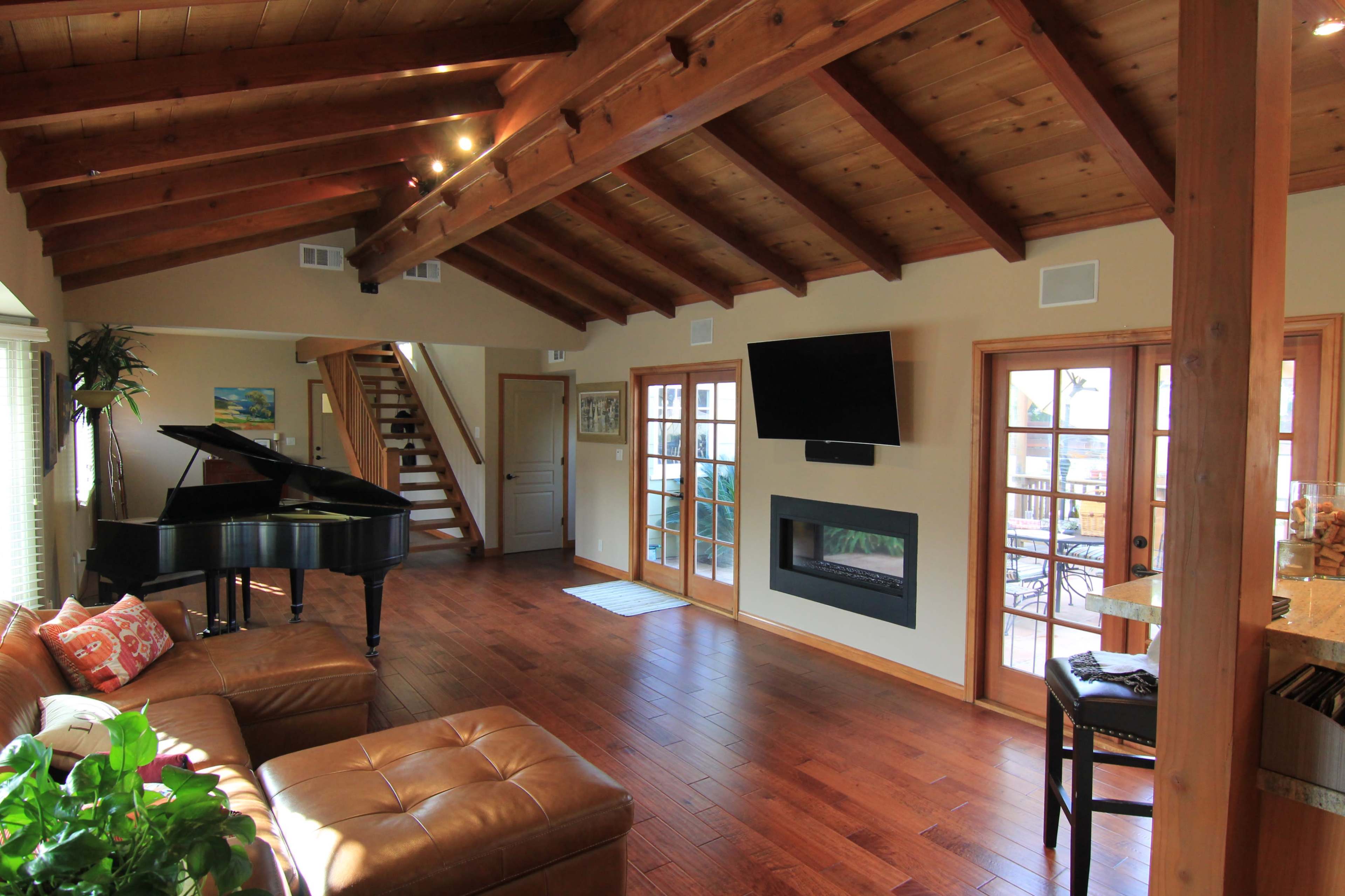 A spacious living room with wooden beams, a grand piano, a leather sofa, and a modern fireplace.