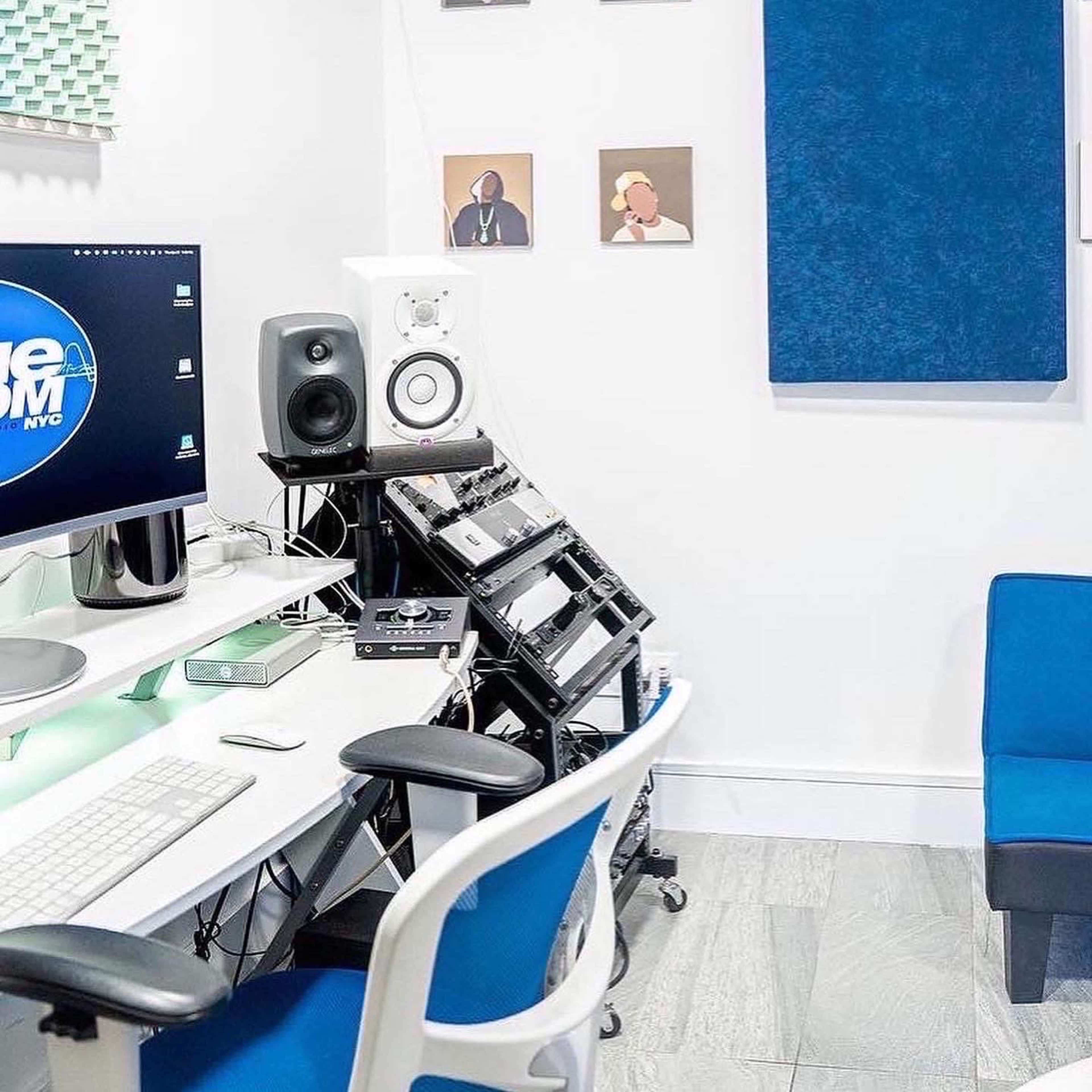 A modern music studio with a computer setup, speakers, and soundproofing panels on the walls.