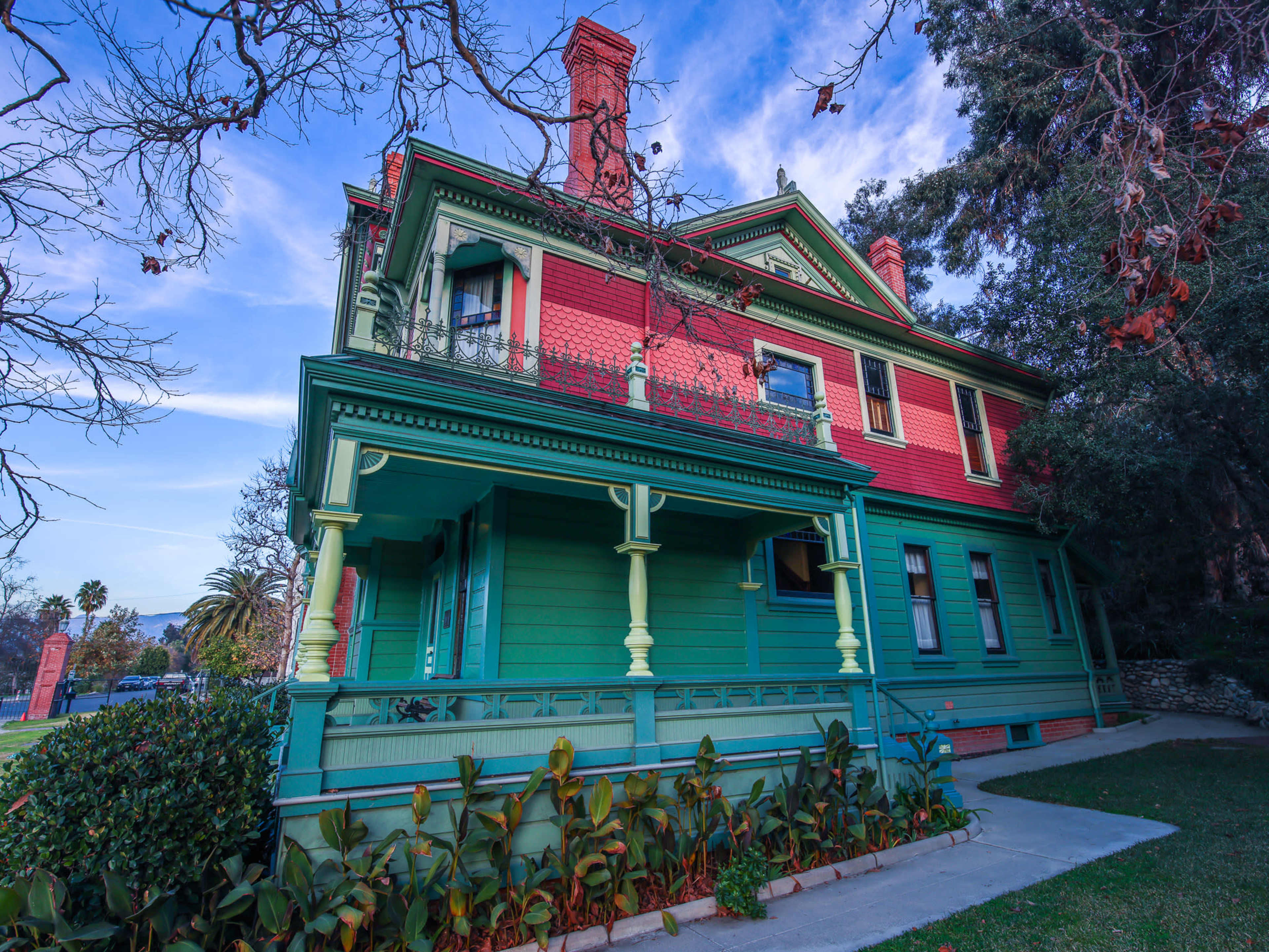 A two-story Victorian house with a mix of red and green exterior paint, featuring a front porch and decorative details.