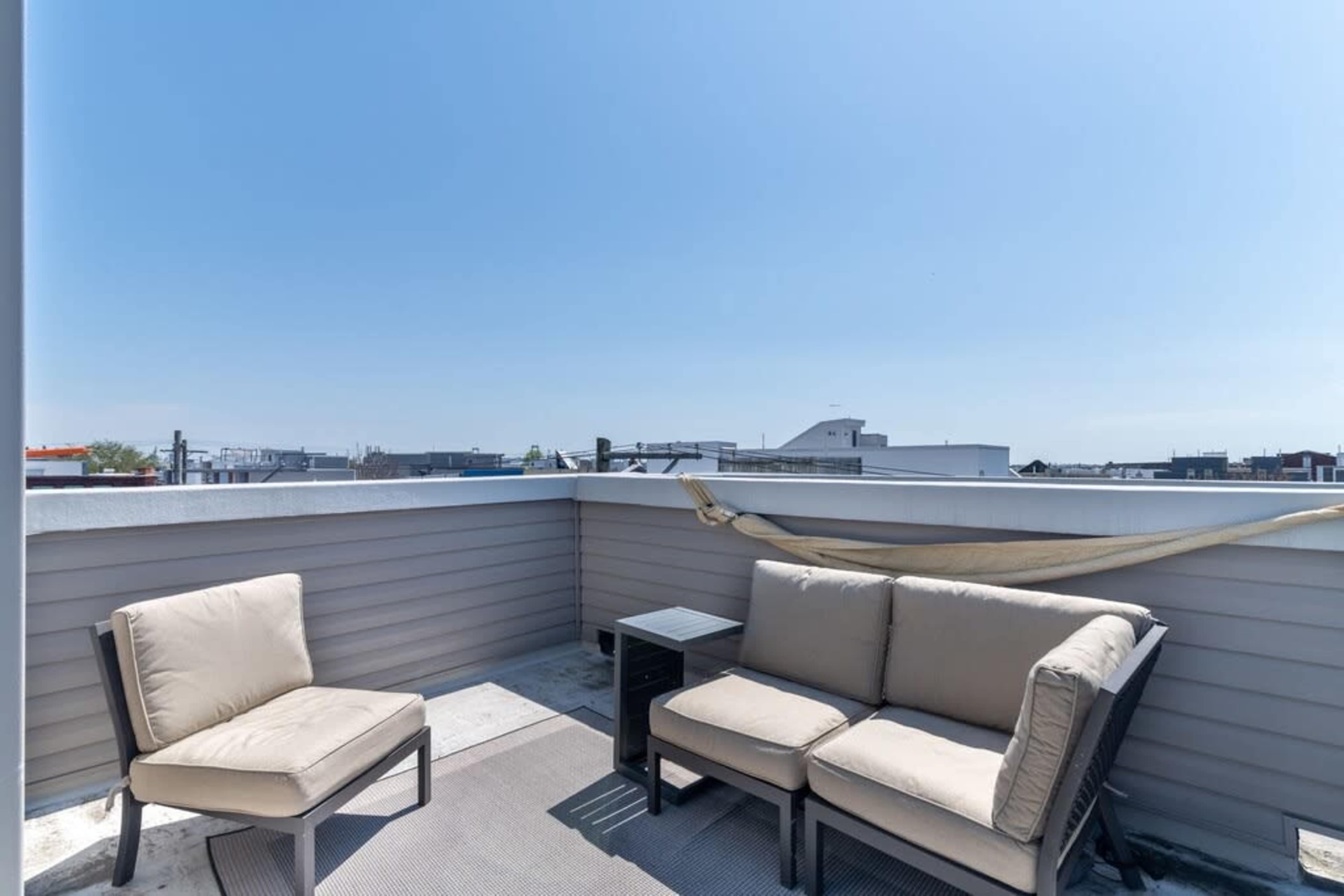 A rooftop terrace features two beige chairs and a small black table with a clear blue sky in the background.