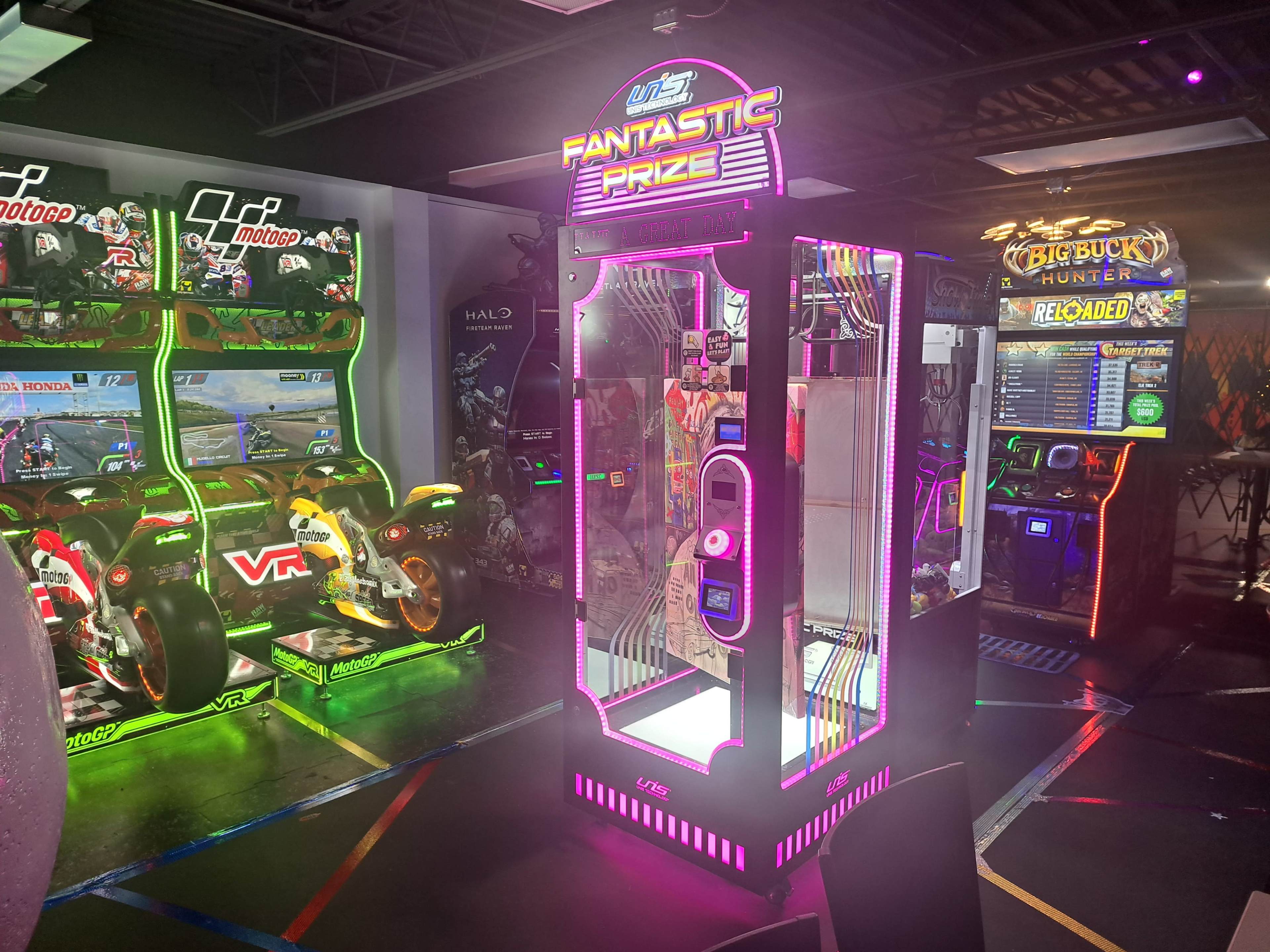 The image shows a vibrant arcade with a prize claw machine illuminated by colorful lights, surrounded by various arcade games.