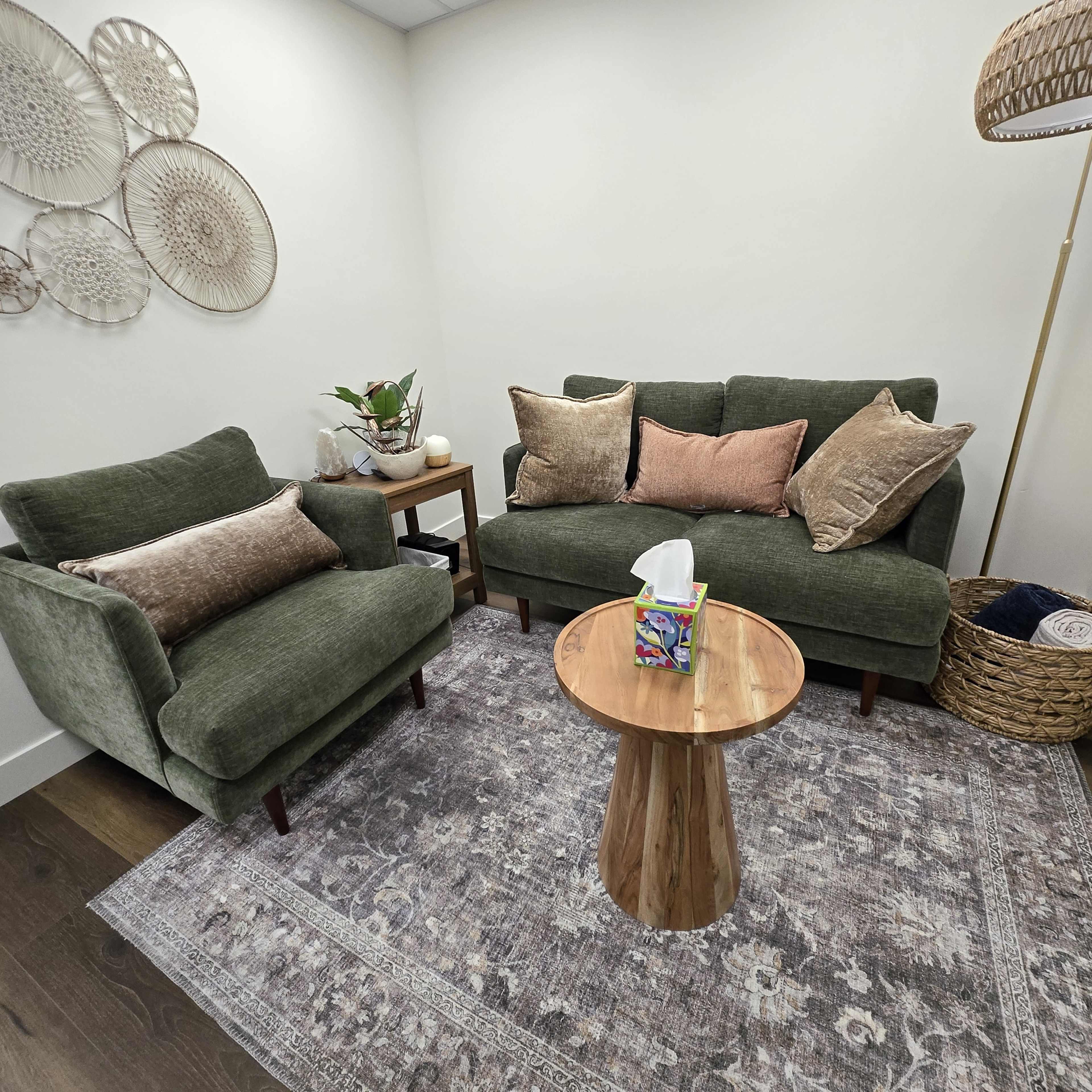 The image shows a cozy seating area with two green sofas, a wooden coffee table, and decorative wall hangings.