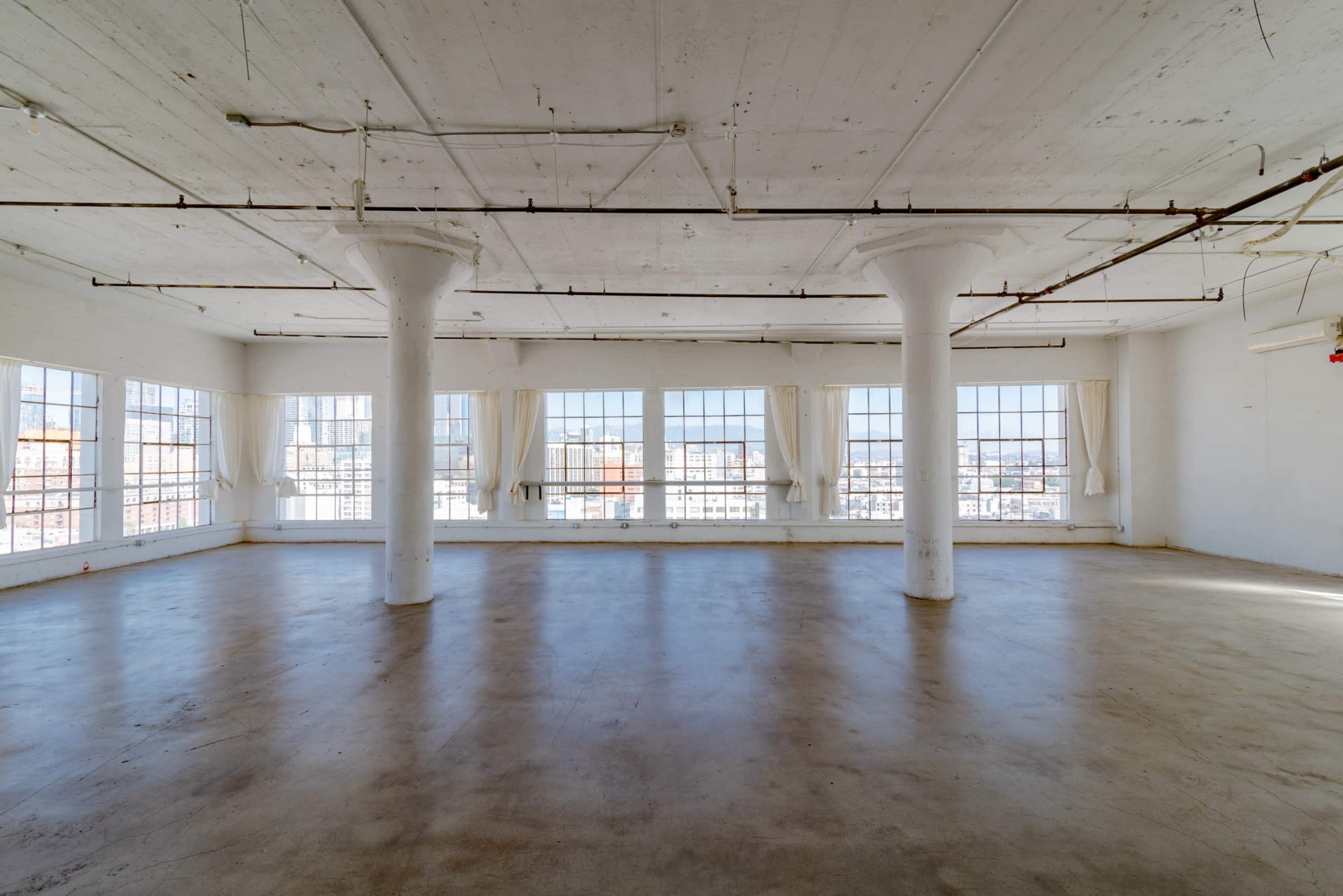 An empty, well-lit industrial space with large windows and concrete flooring.