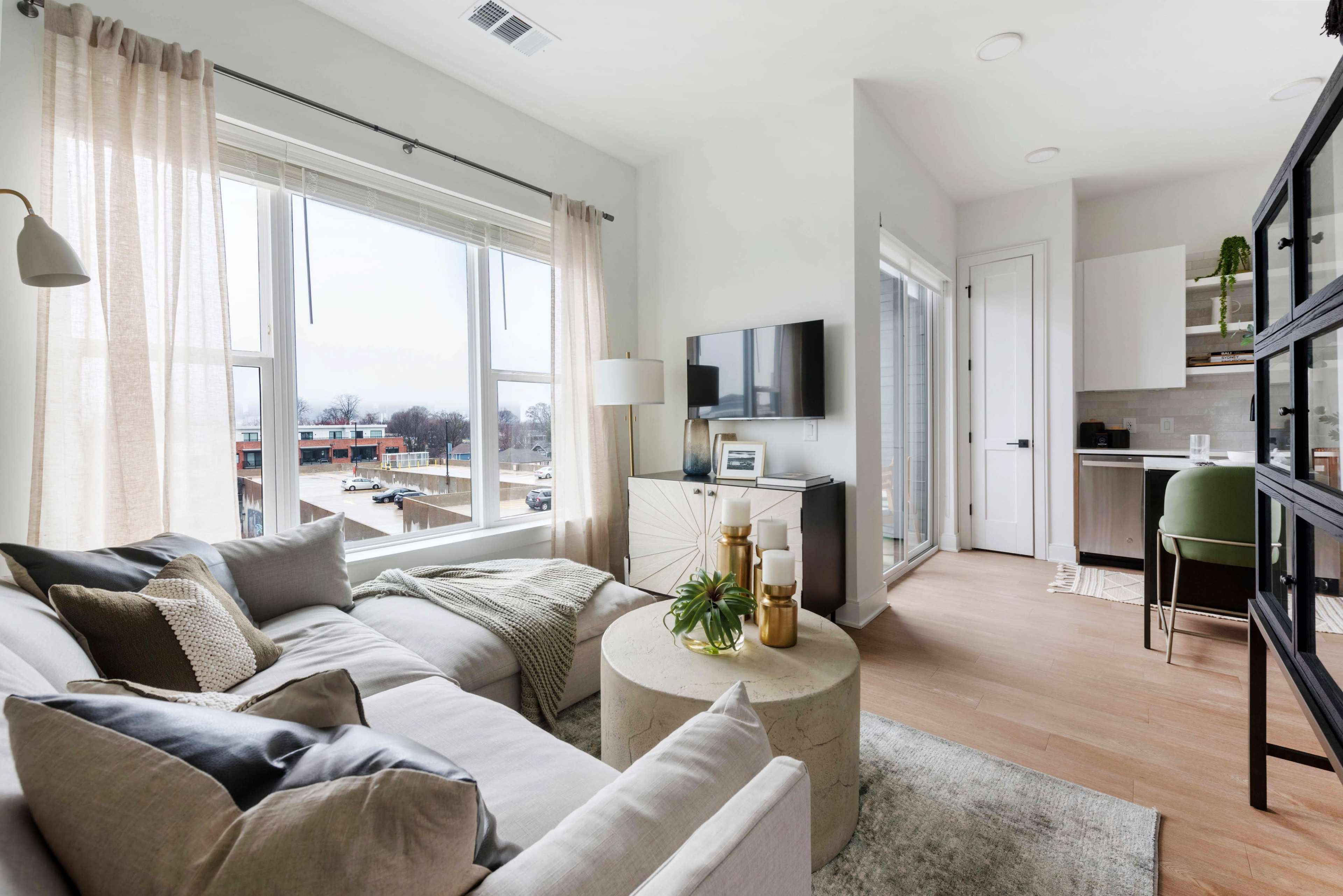A modern living room features a light-colored sofa, a round coffee table, and large windows allowing natural light to illuminate the space.
