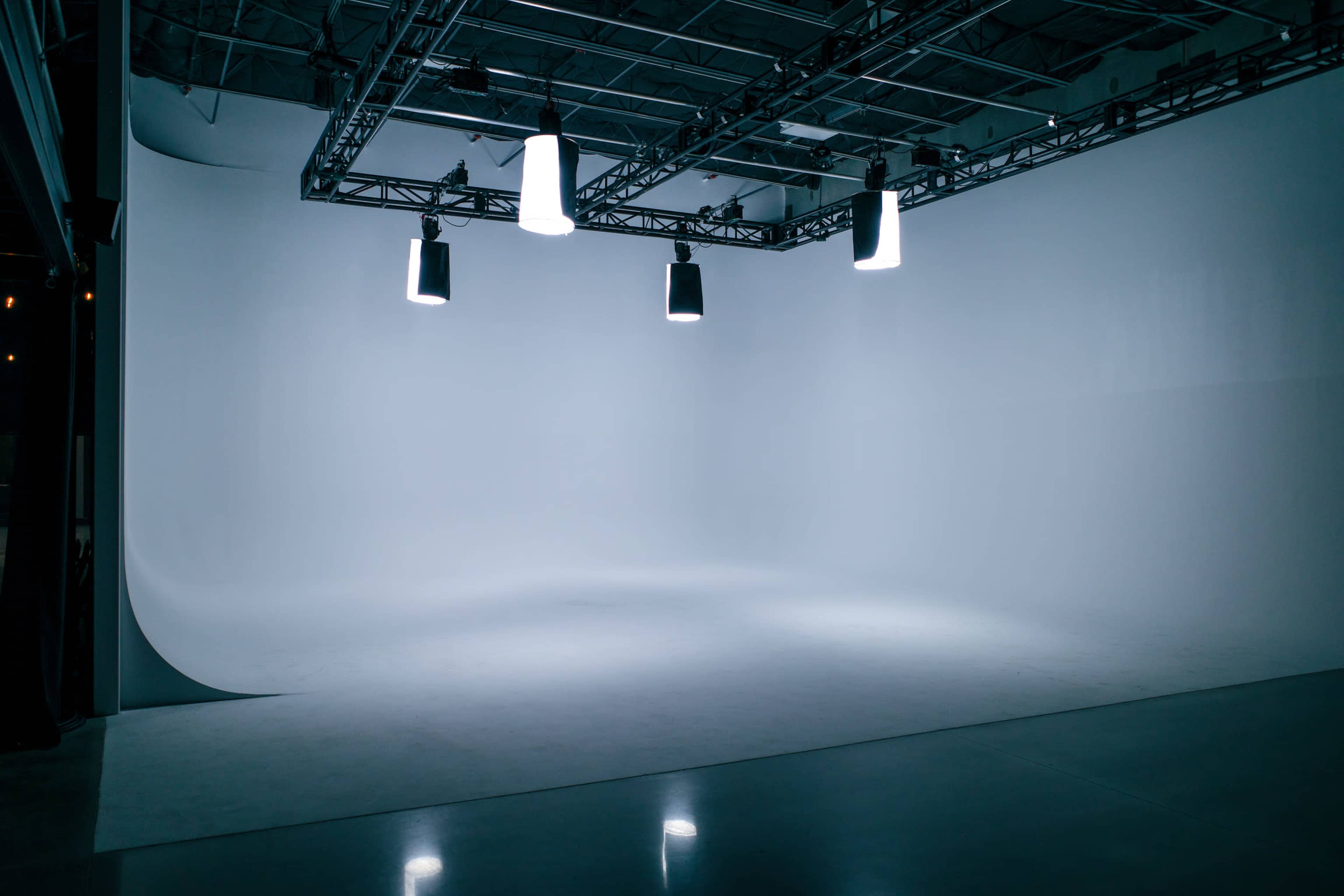 The image shows a large, empty studio space with bright overhead lights and a seamless white background.