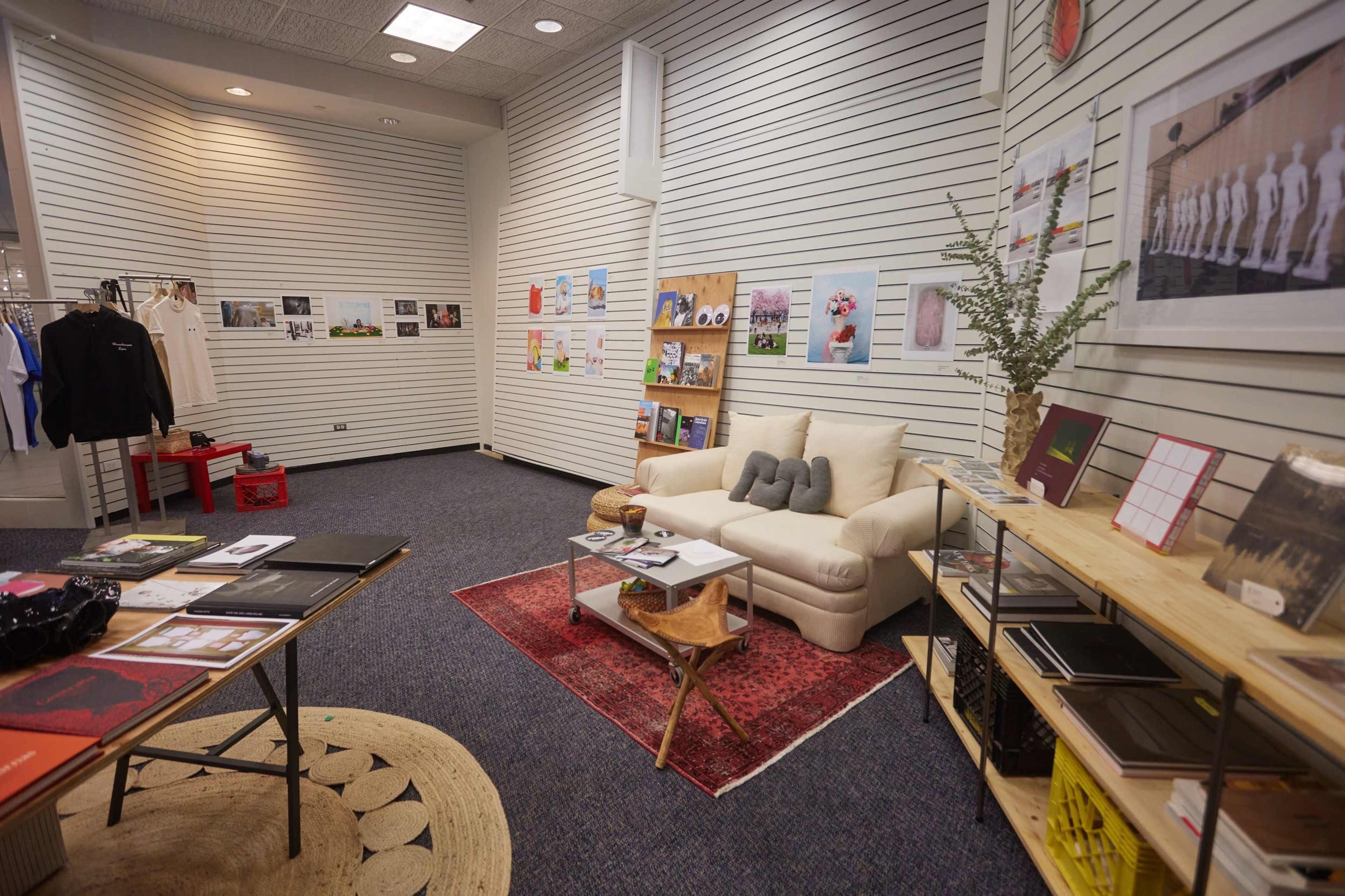 The image shows a cozy room with a sofa, a coffee table, display shelves, and walls adorned with artwork and photographs.