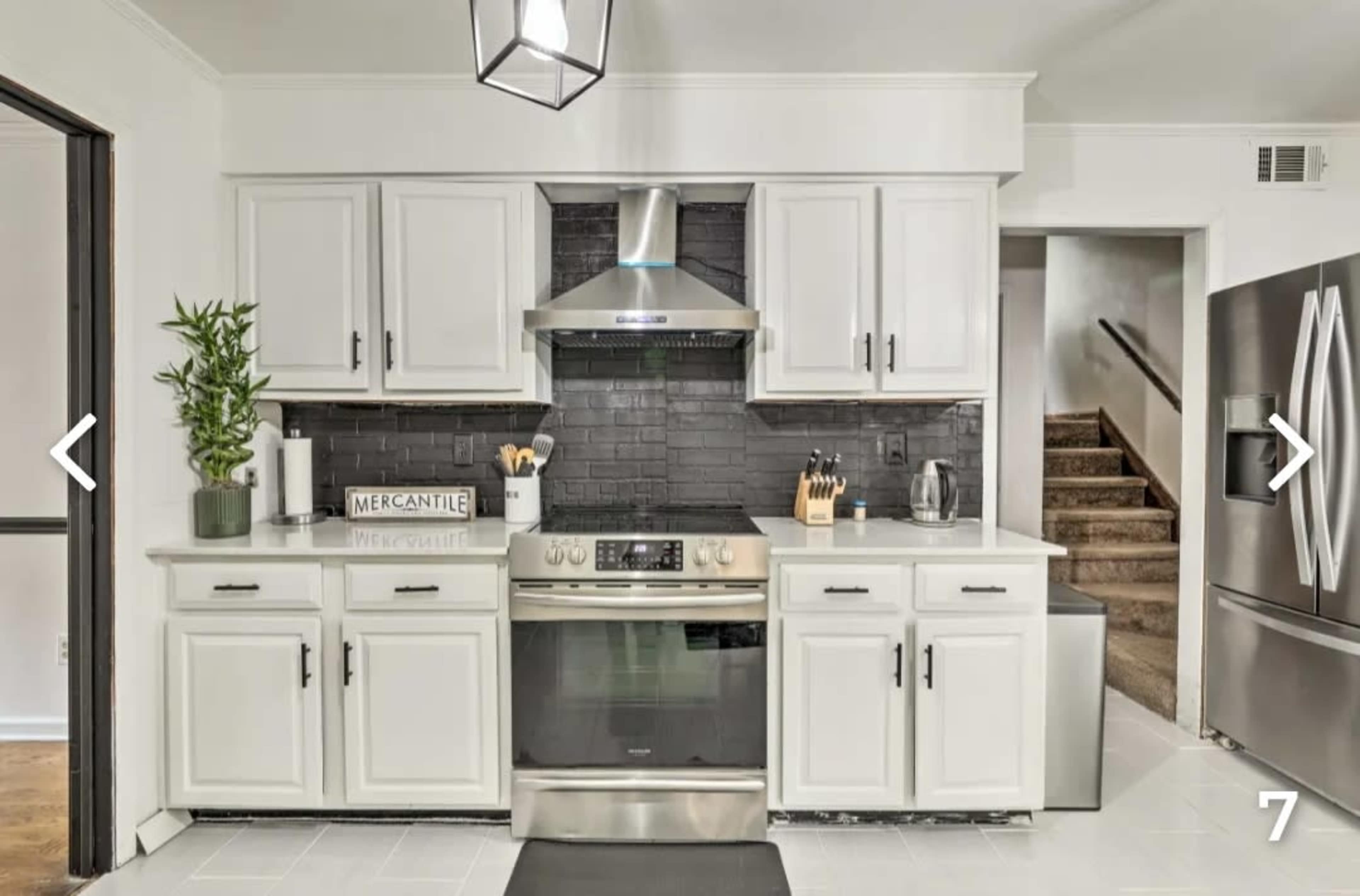 The kitchen features white cabinetry, a stainless steel stove, a black backsplash, and a modern pendant light.