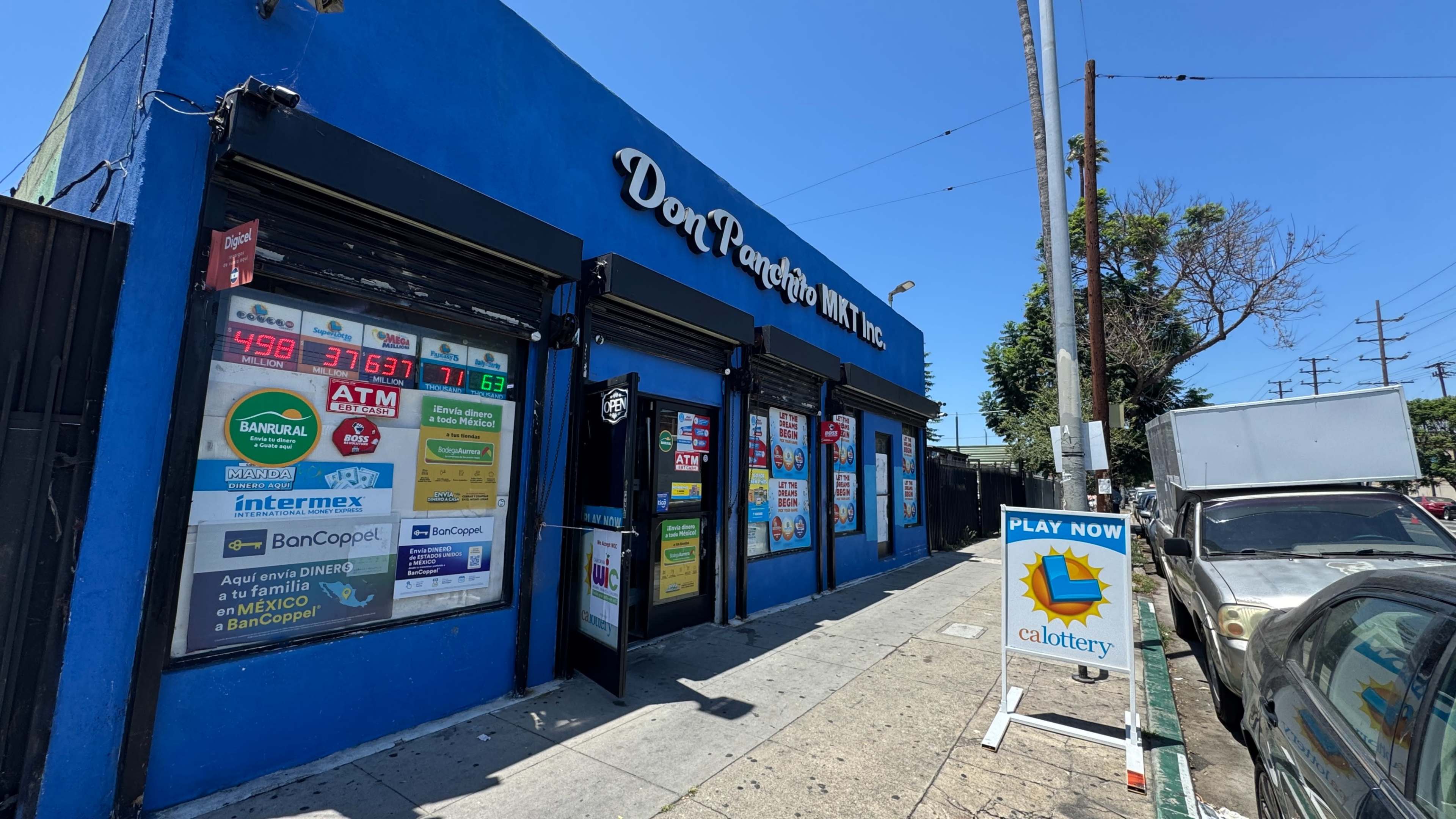 The image shows a brightly colored blue storefront with various signs, including advertisements and lottery promotions, located on a city street.