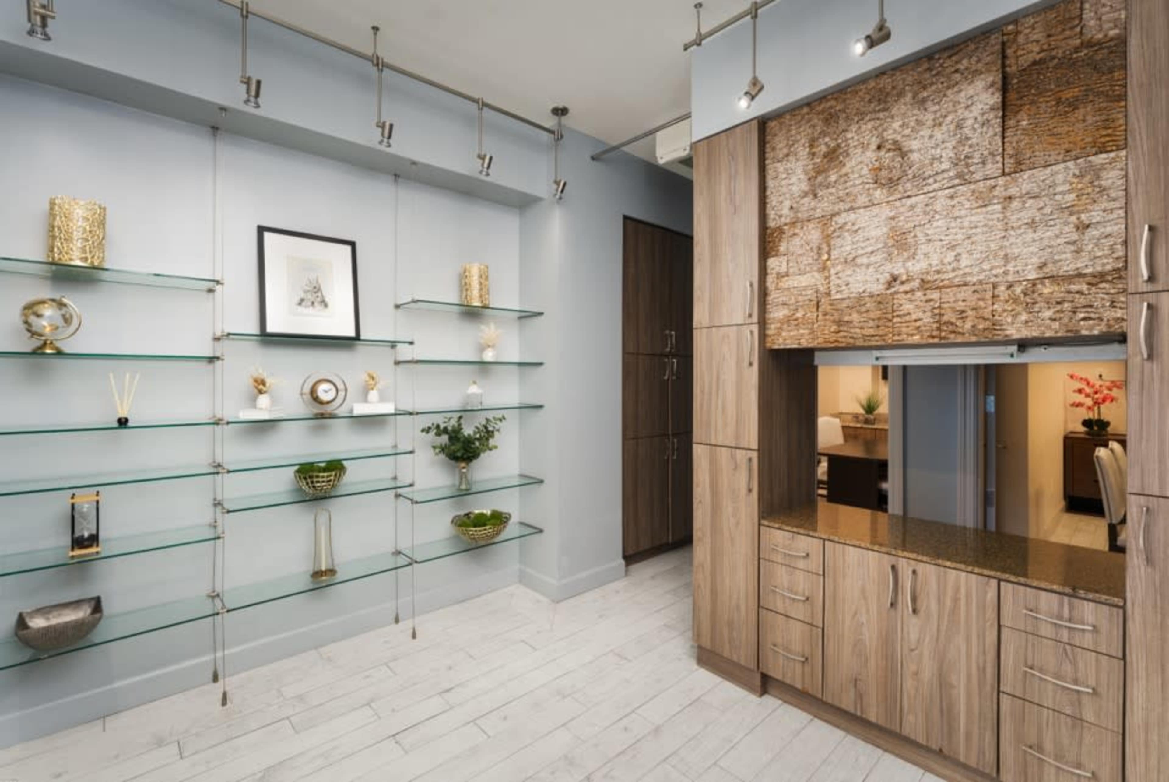 The image shows a modern interior space featuring glass shelves on one wall and a wooden cabinetry unit with a textured centerpiece on another.
