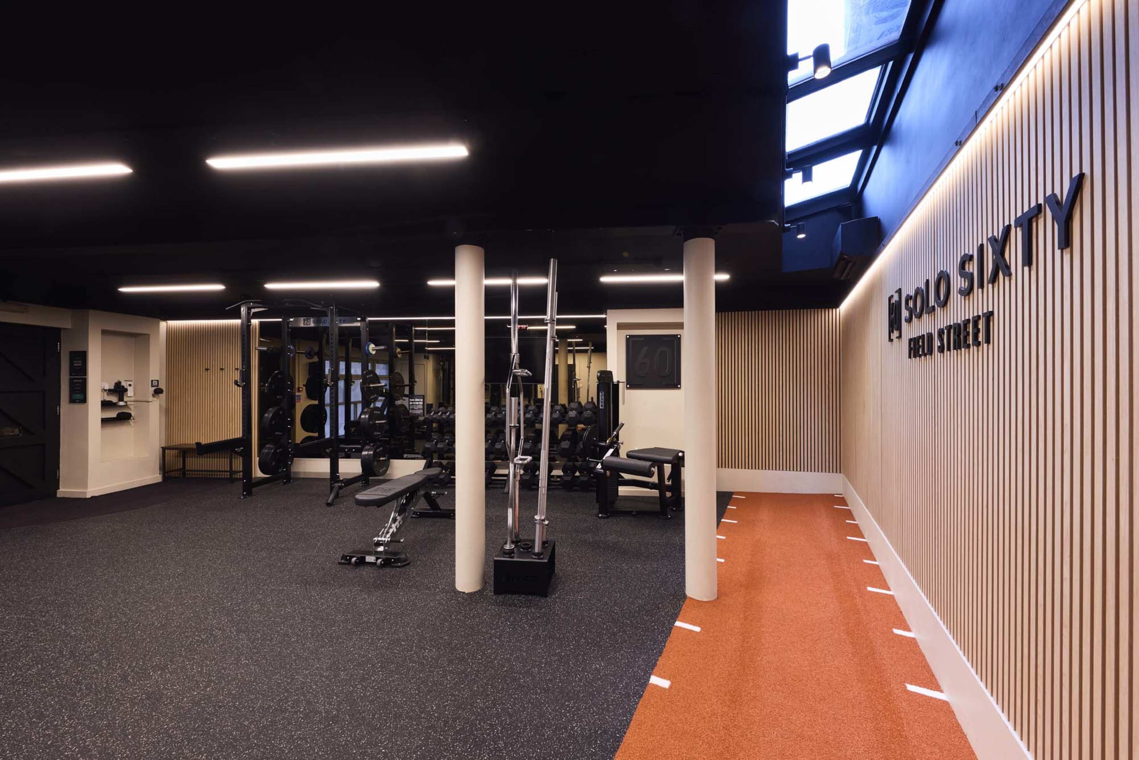 The image shows a modern gym with workout equipment, black flooring, and an accent wall with the text "SOLO SIXTY" displayed prominently.