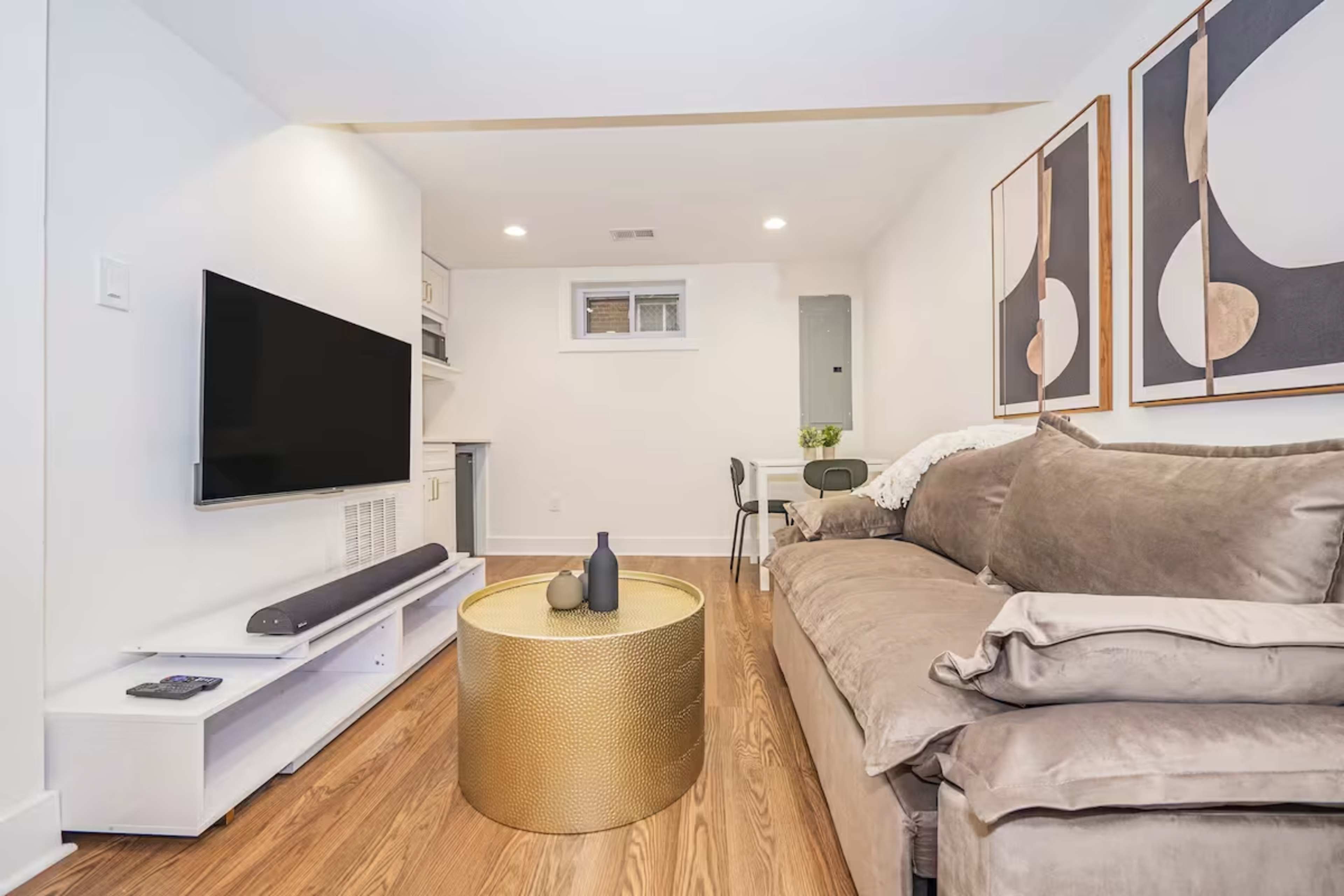 The image shows a modern living space with a large sofa, a round gold coffee table, a wall-mounted television, and abstract artwork.