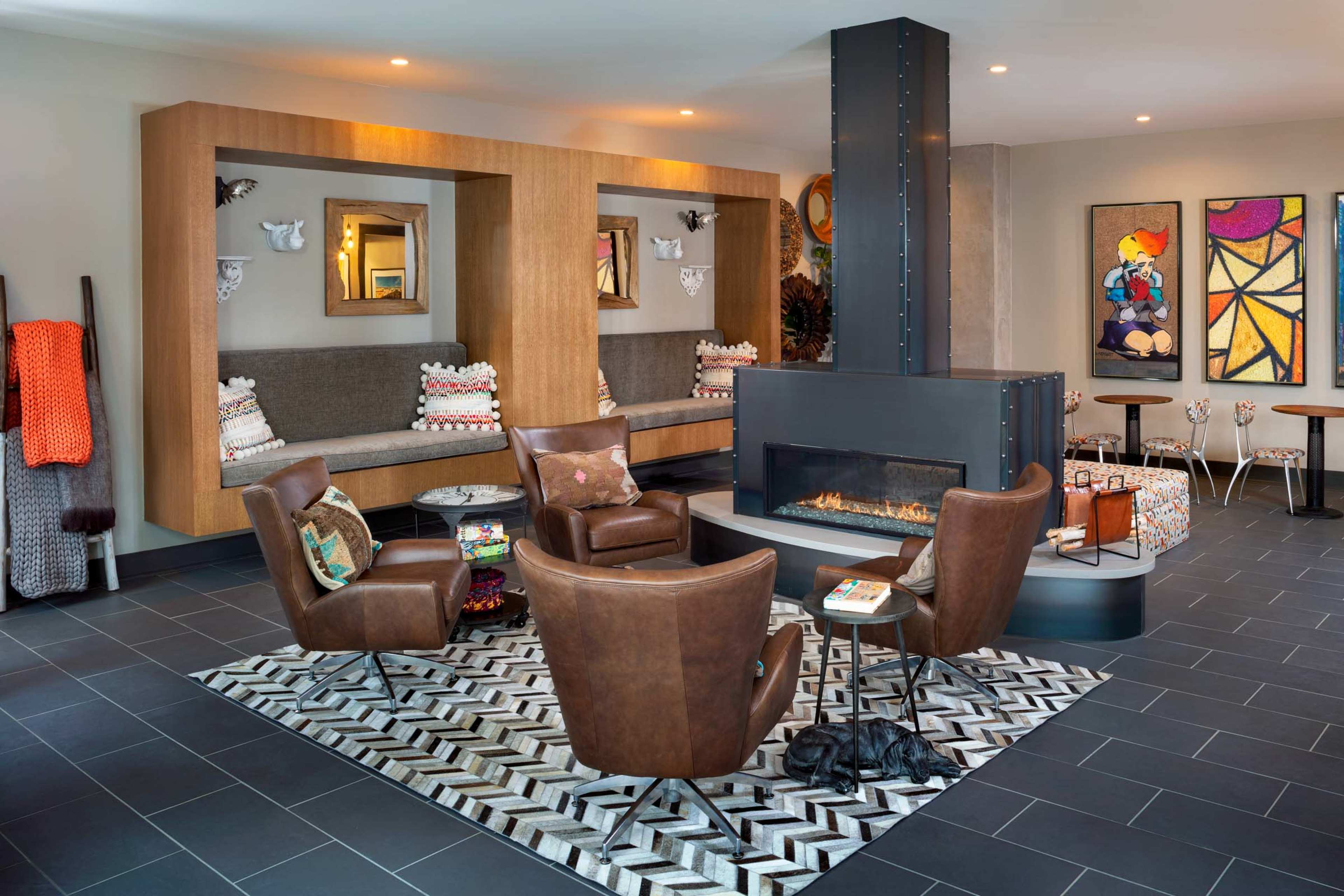 The image shows a modern living room with a central fireplace, surrounded by four brown leather chairs and a patterned rug on a tiled floor.