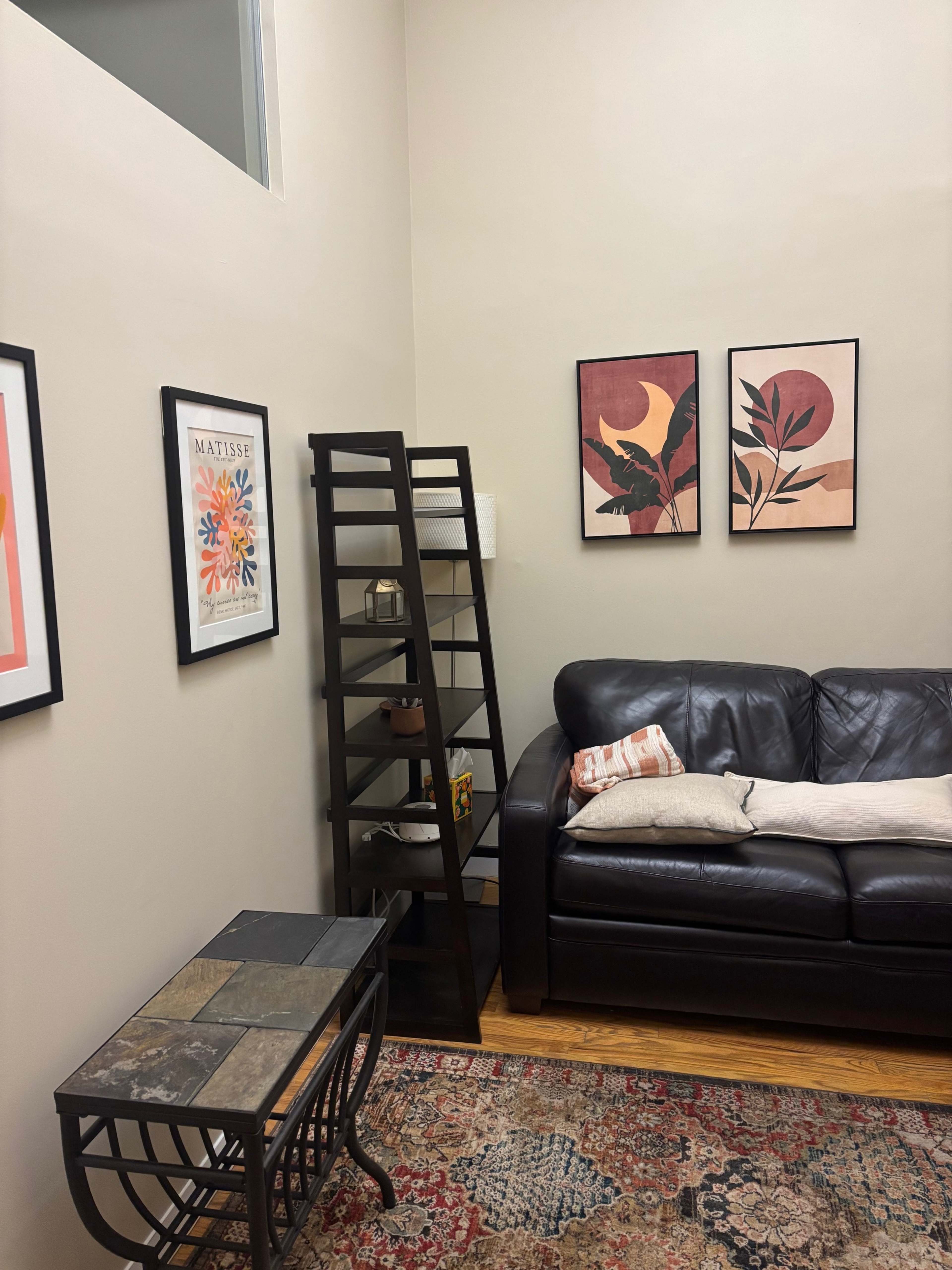 A cozy living room features a black leather sofa, a decorative ladder shelf, and framed artwork on the walls against a neutral backdrop.