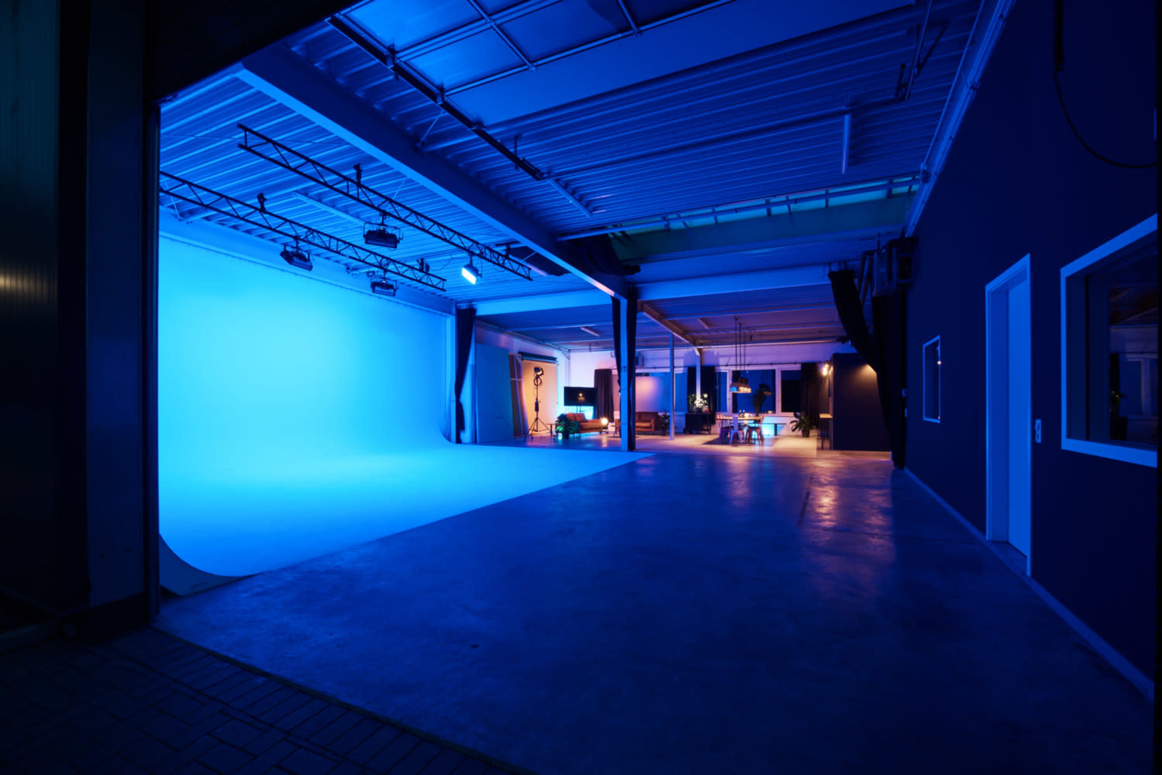 The image shows a spacious studio with a blue backdrop, bright lights, and a modern setting featuring a work area and seating.