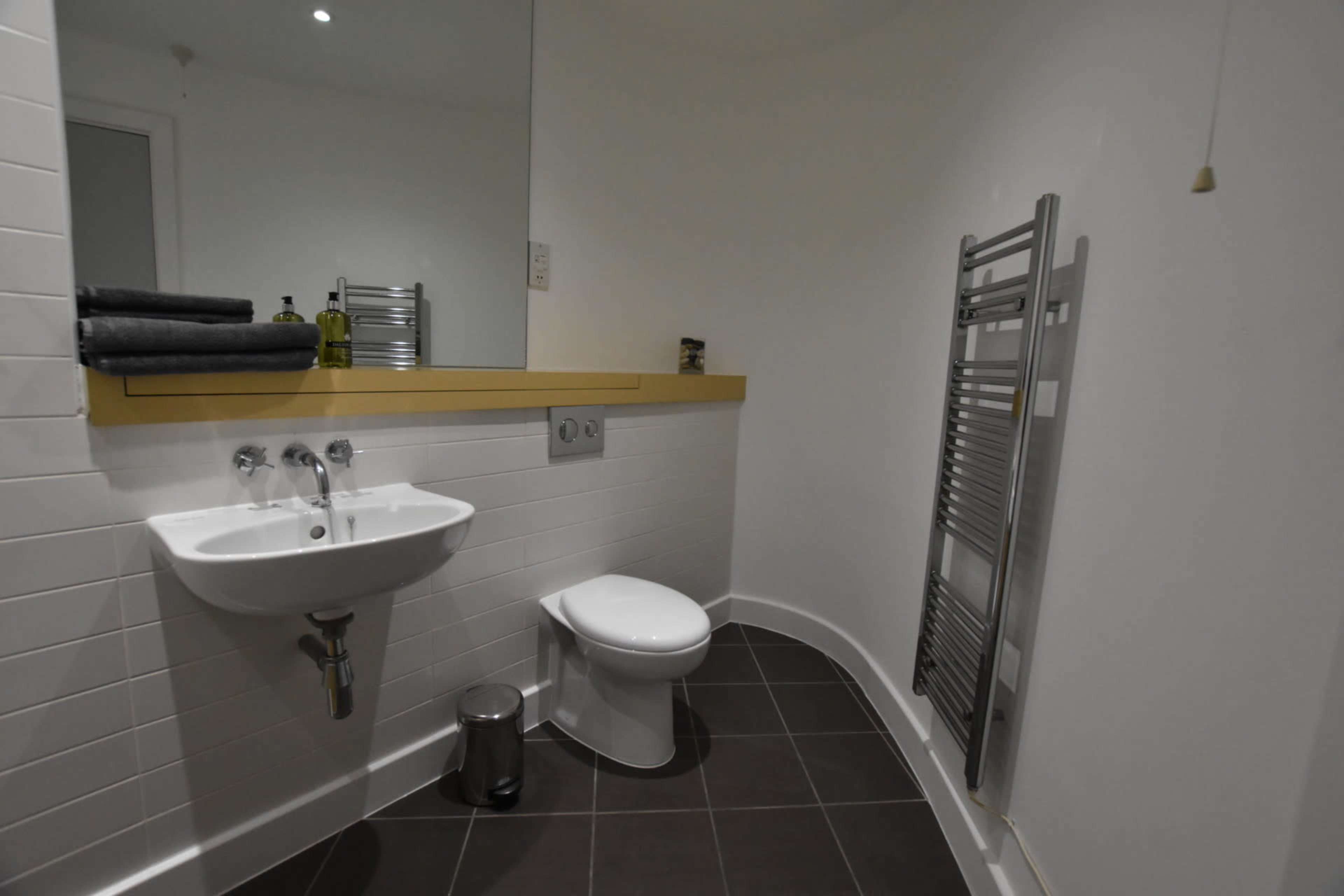 A modern bathroom featuring a sink, toilet, and a heated towel rack against a light-colored wall.
