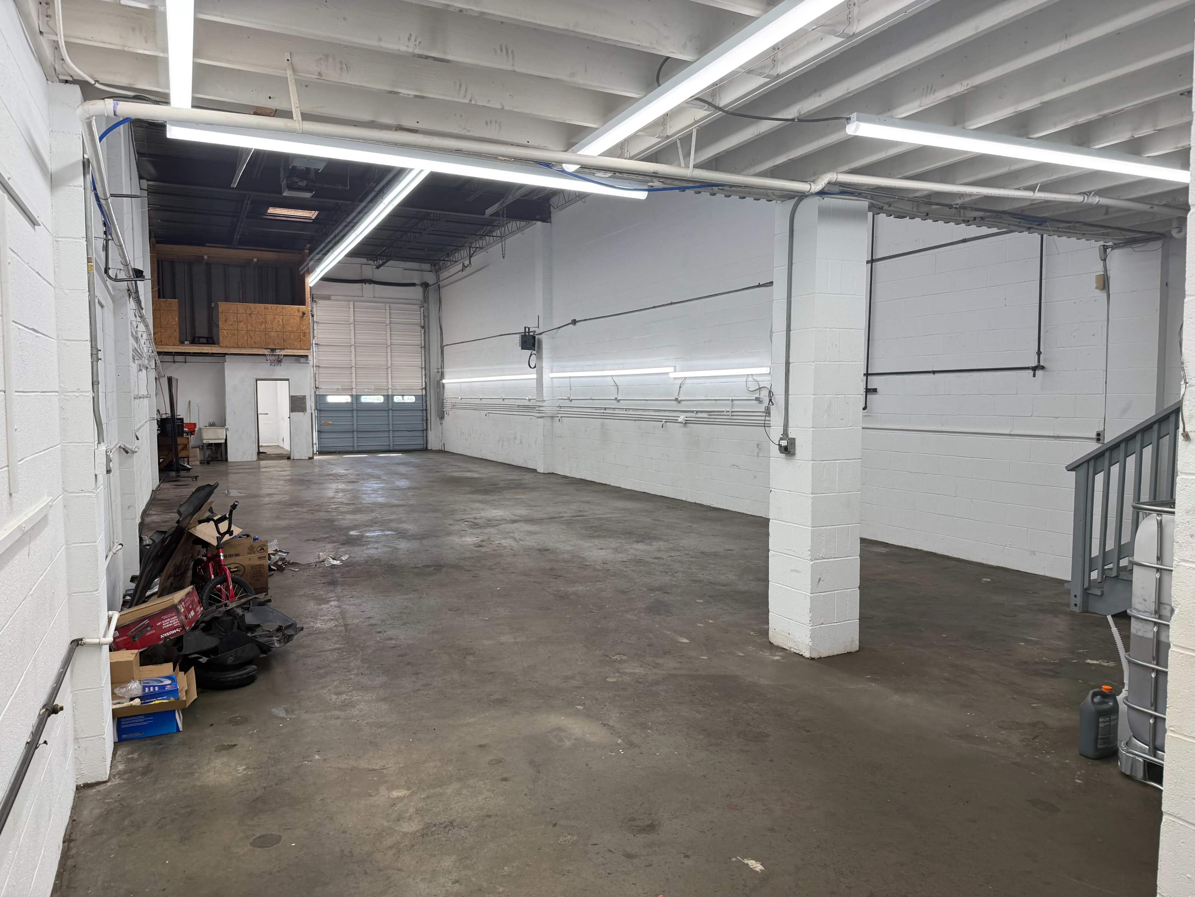 The image shows a spacious, empty warehouse with concrete flooring and fluorescent lights on the ceiling.