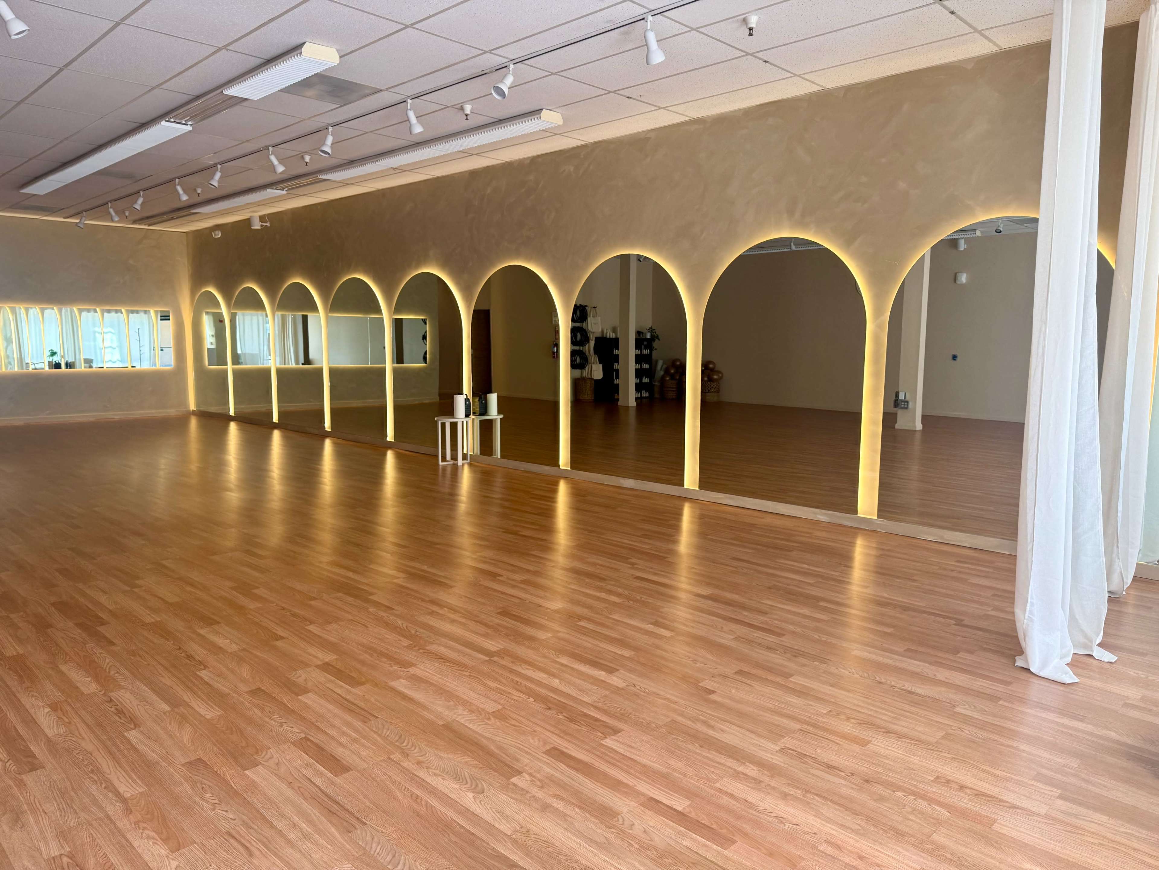 The image shows a spacious, well-lit studio featuring arched mirrors along one wall and wooden flooring.