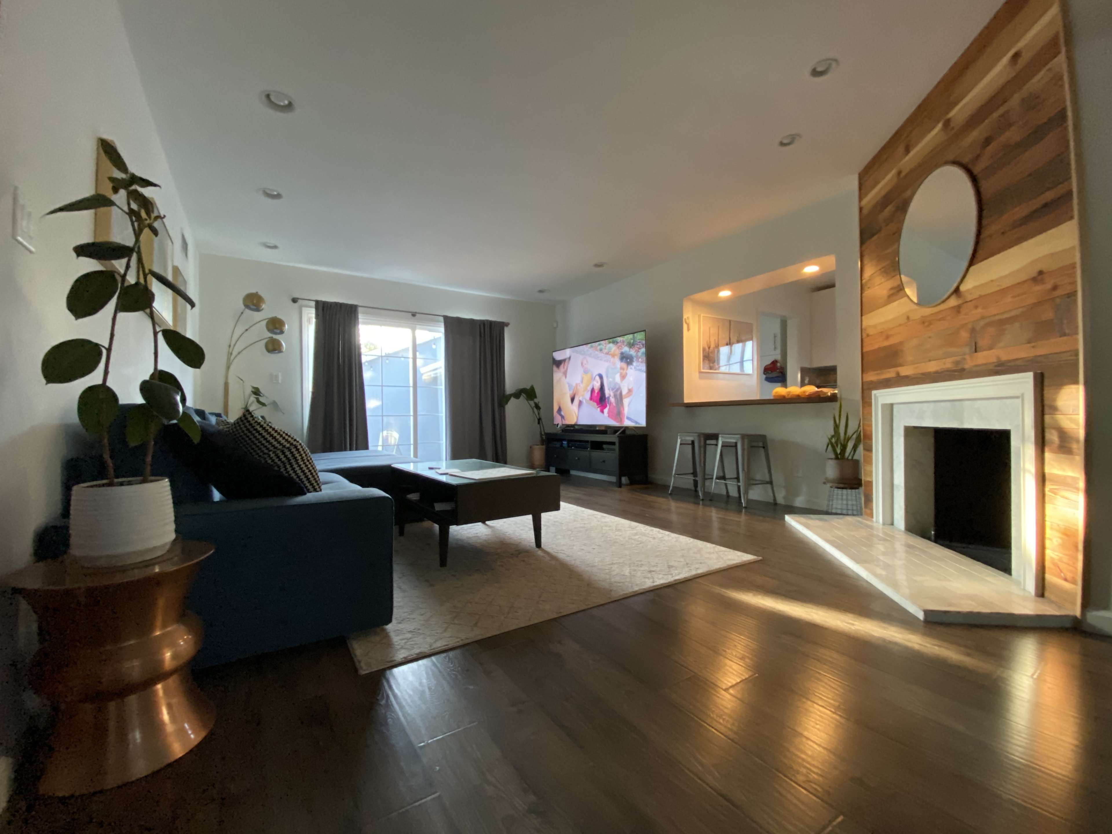 A living room with a blue couch, a coffee table, a television against one wall, and a fireplace with a circular mirror above it.