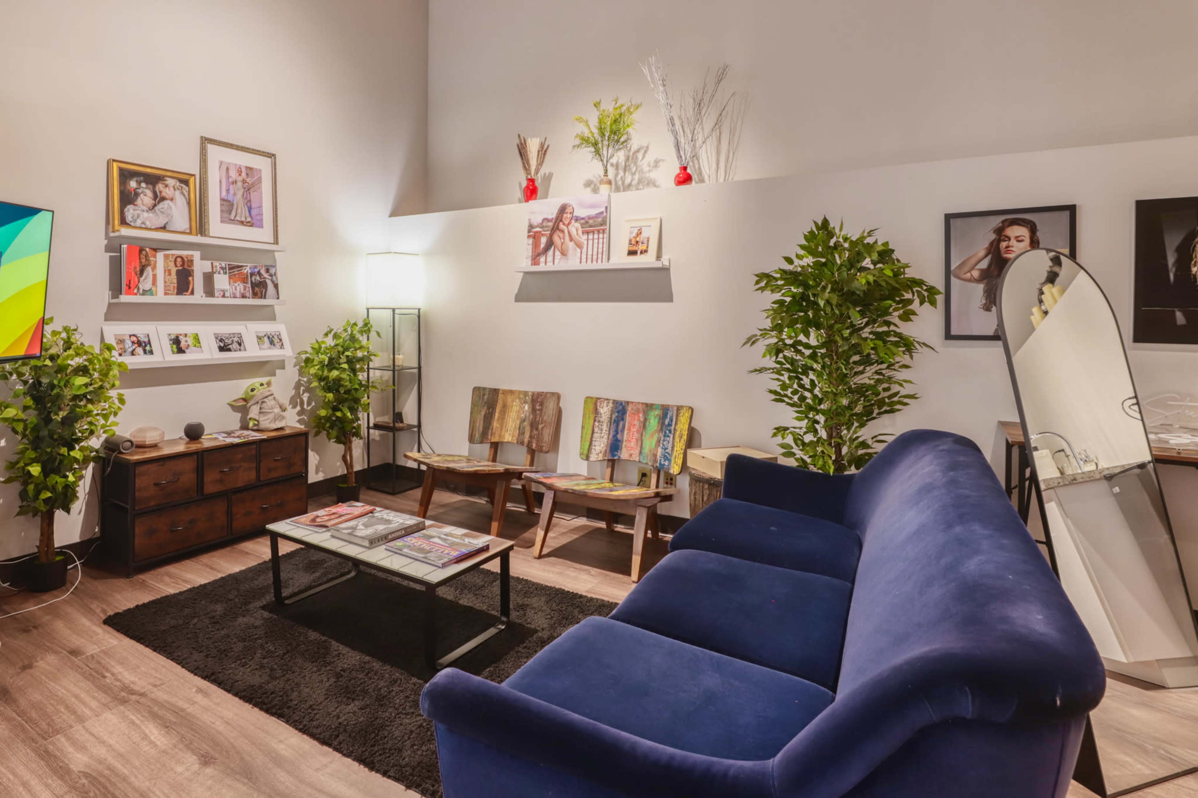 The image shows a modern living room with a blue sofa, a coffee table, decorative plants, and various framed artworks on the walls.
