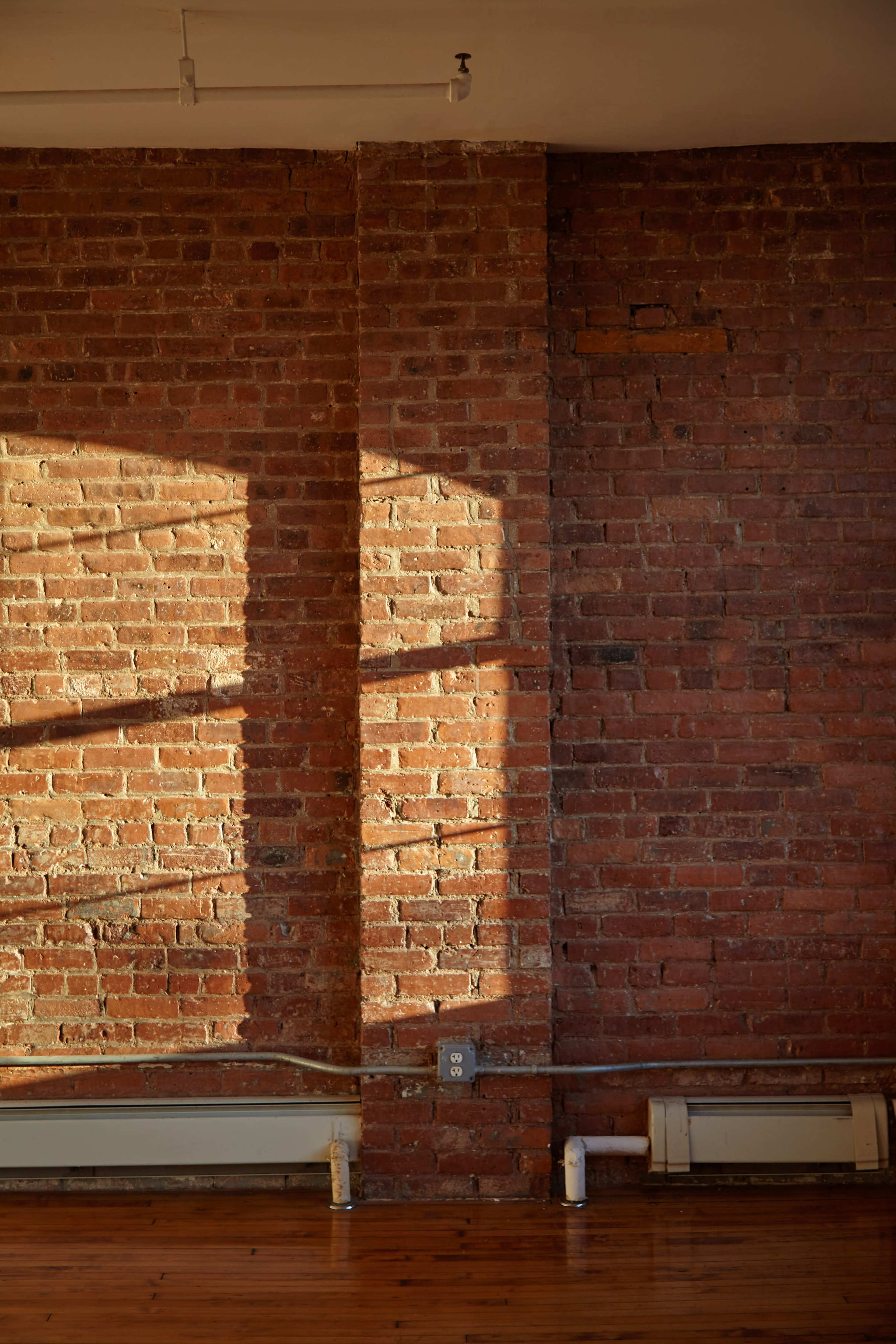 A well-lit interior featuring a brick wall with subtle shadows cast by sunlight.