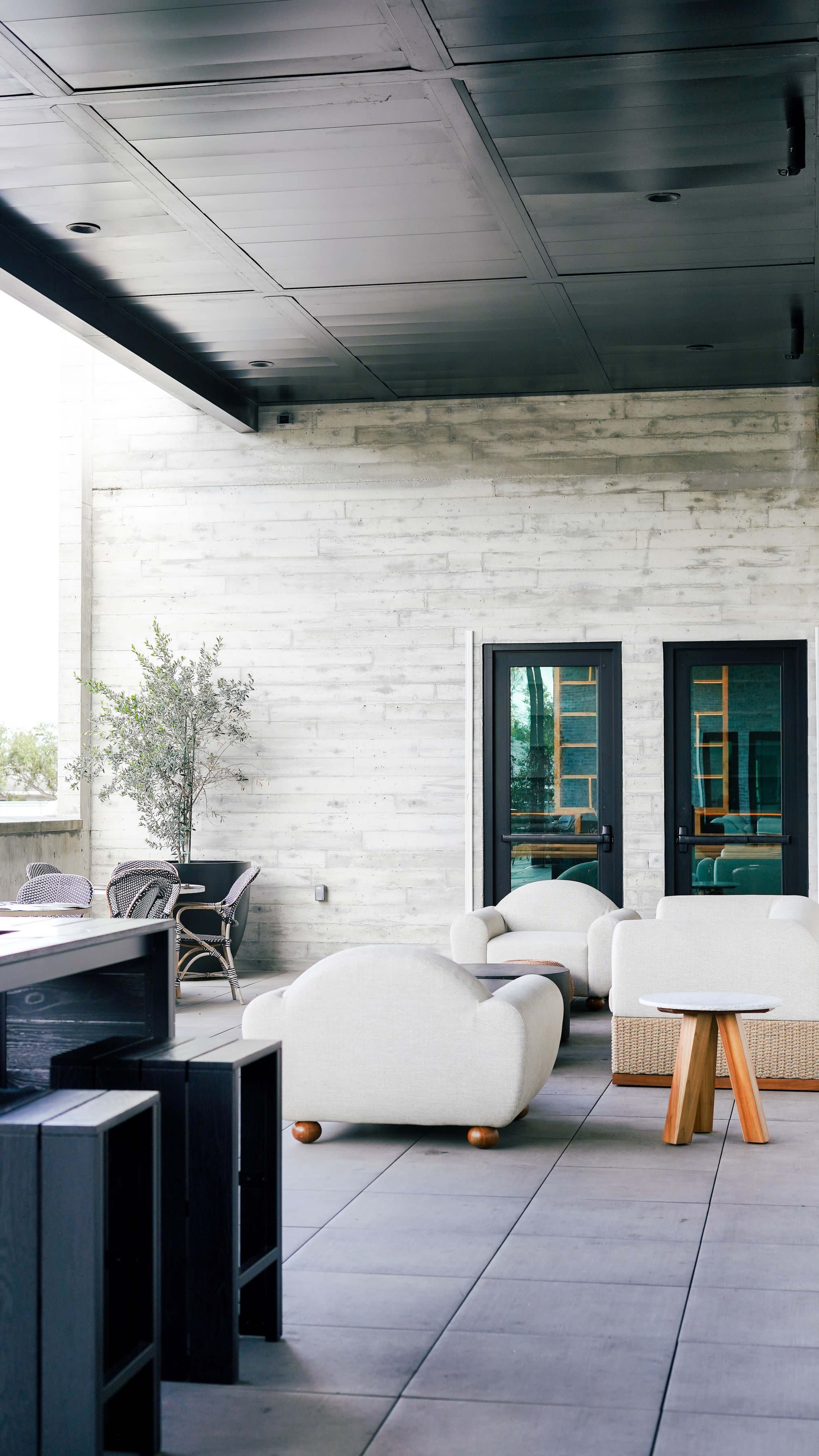 A modern patio features a mix of white and dark furniture, with a seating area and two black doors set against a textured gray wall.