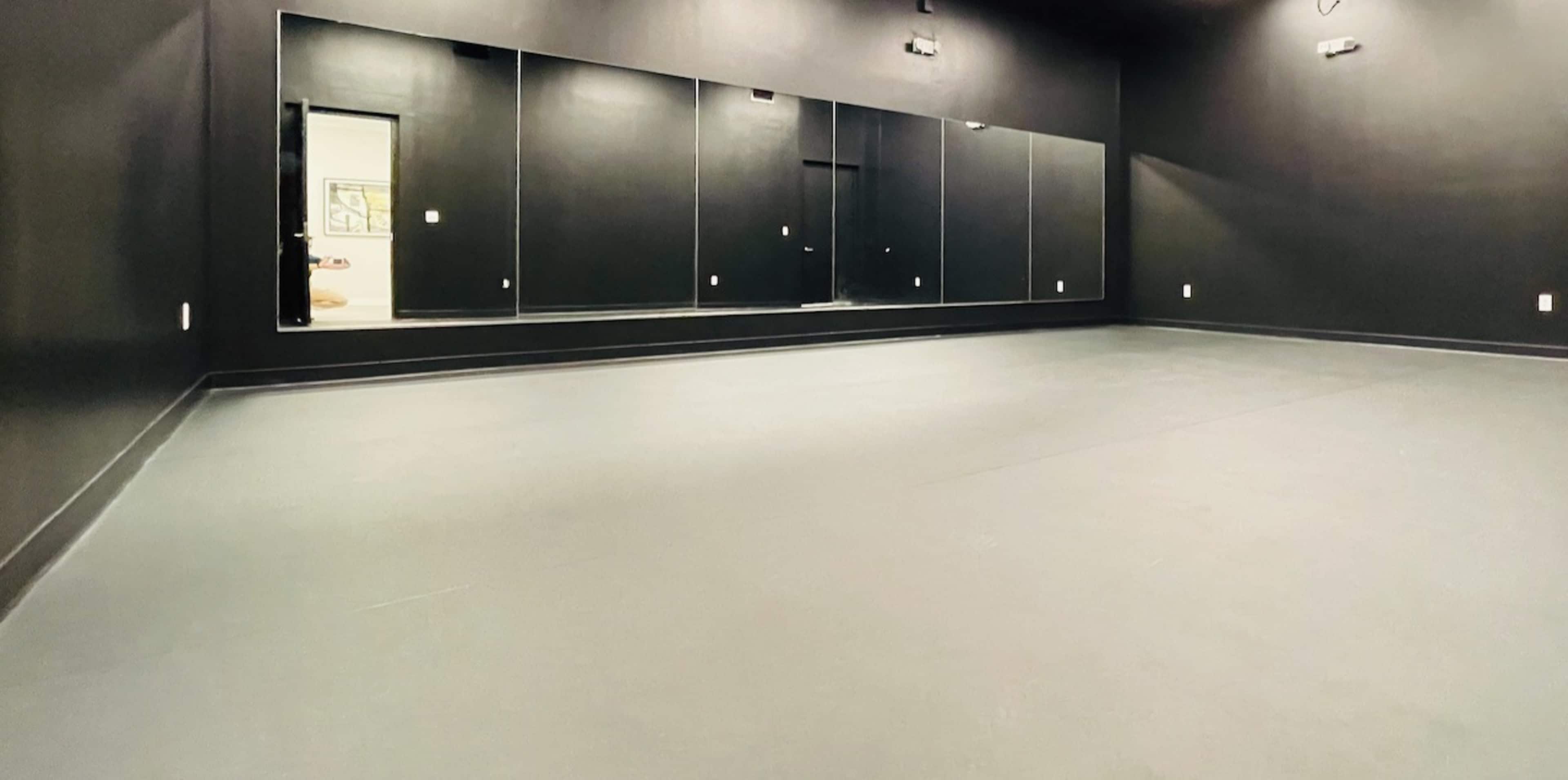 A spacious room with black walls and floor, featuring several mirrors along one side.