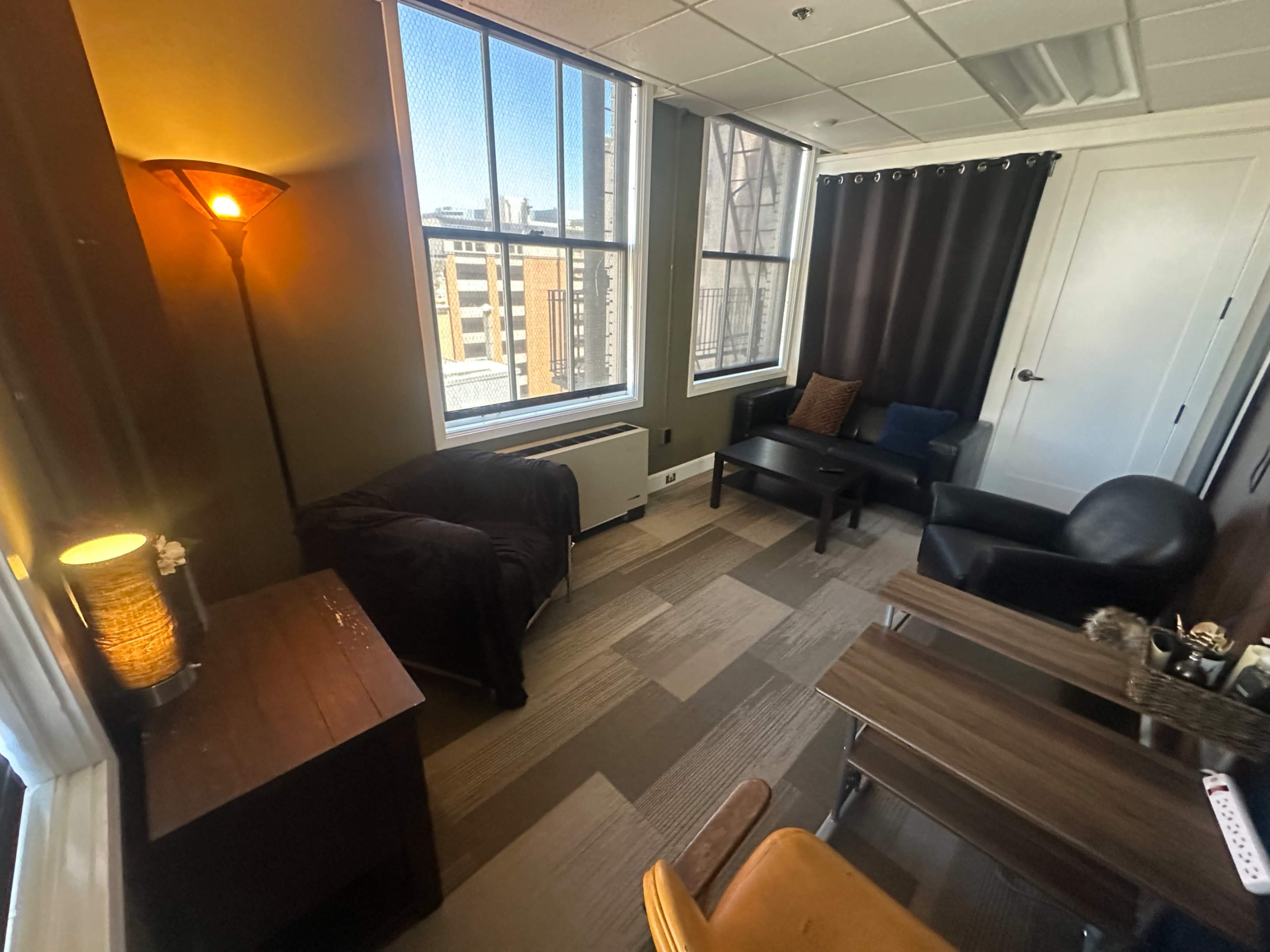 The image shows a small room with large windows, a lamp, a couch, and a coffee table.