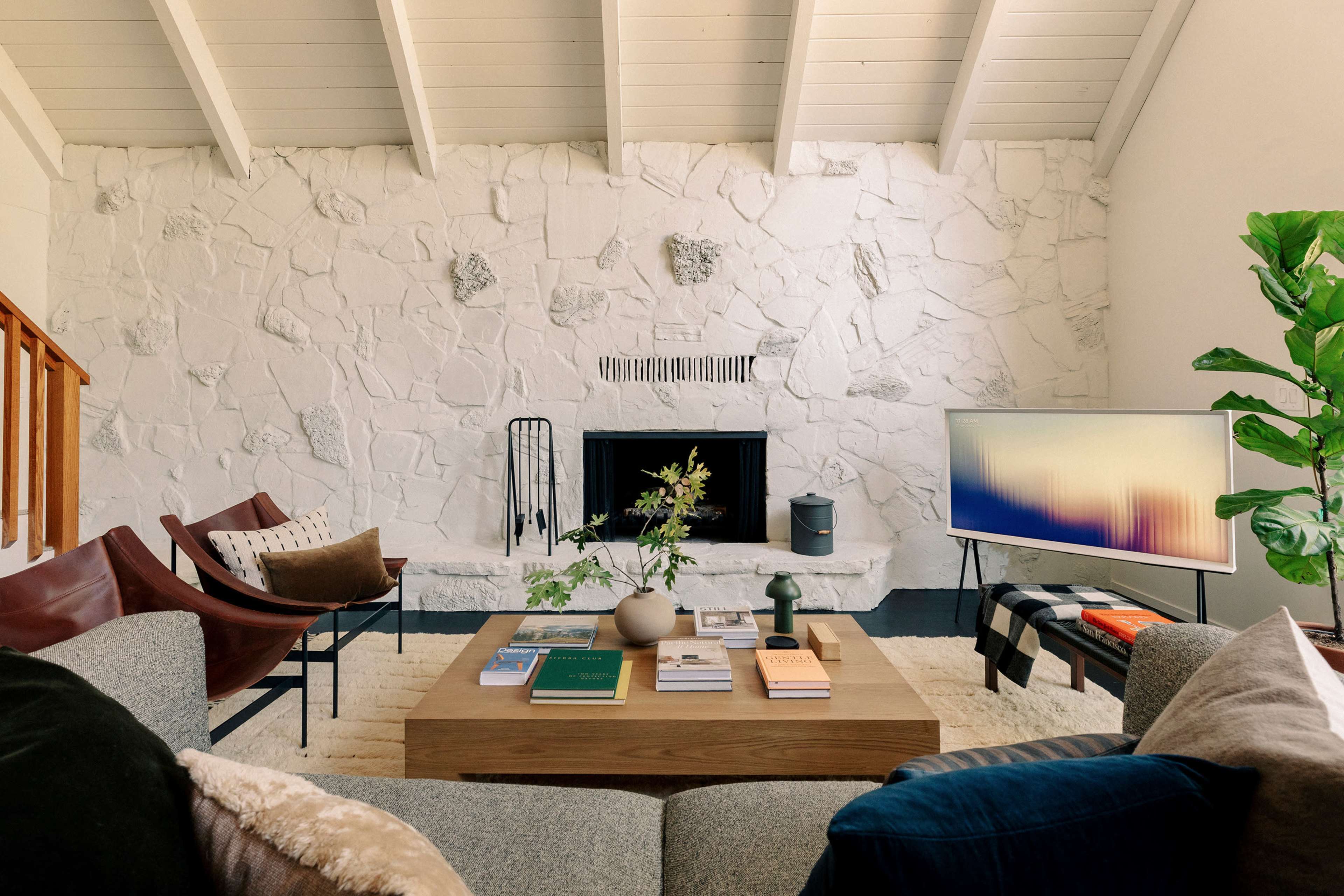 A modern living room features a stone fireplace, wooden accents, and a coffee table surrounded by stylish seating.
