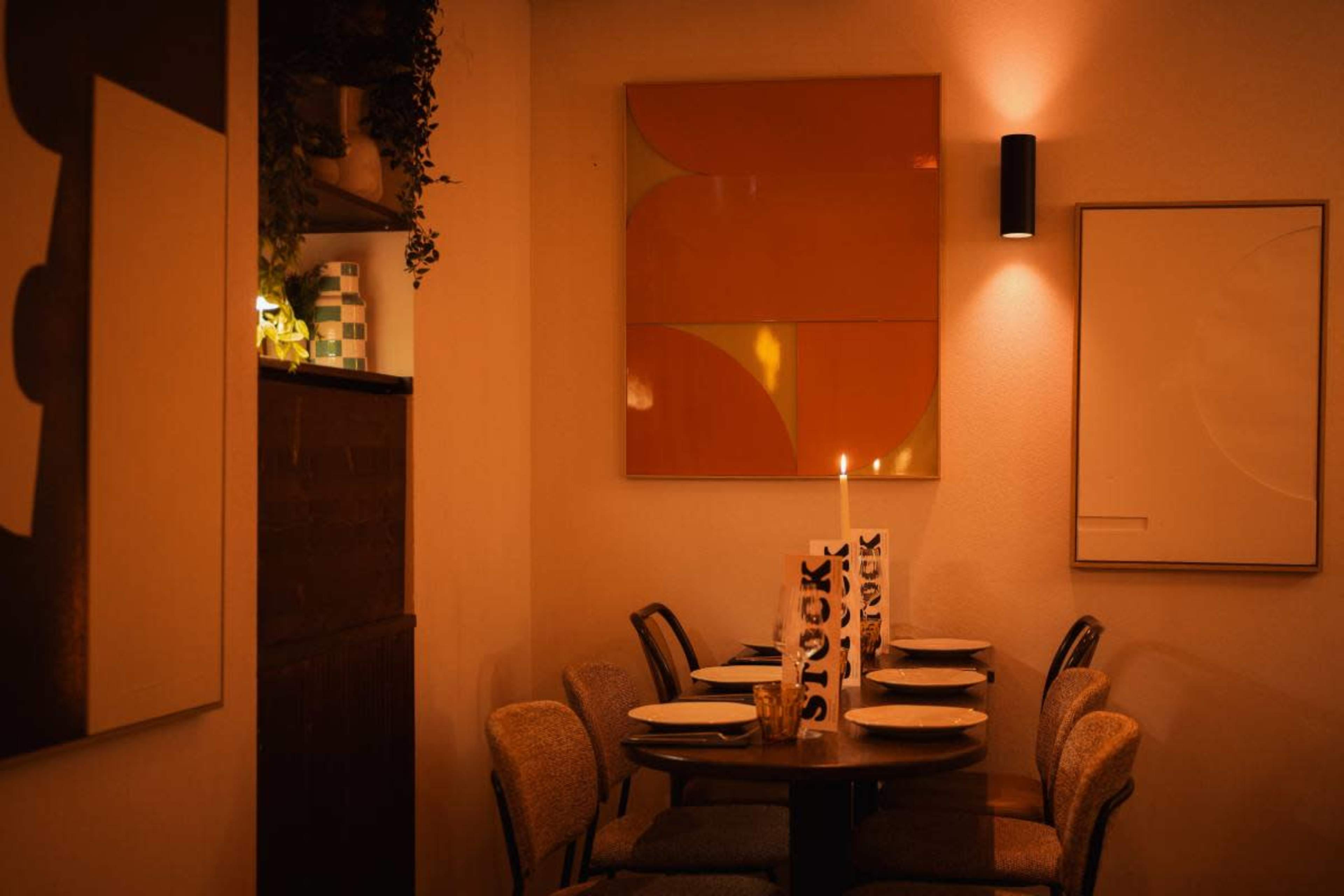 A small dining area features a round table set for four, illuminated by soft lighting and adorned with simple decor and artwork on the walls.