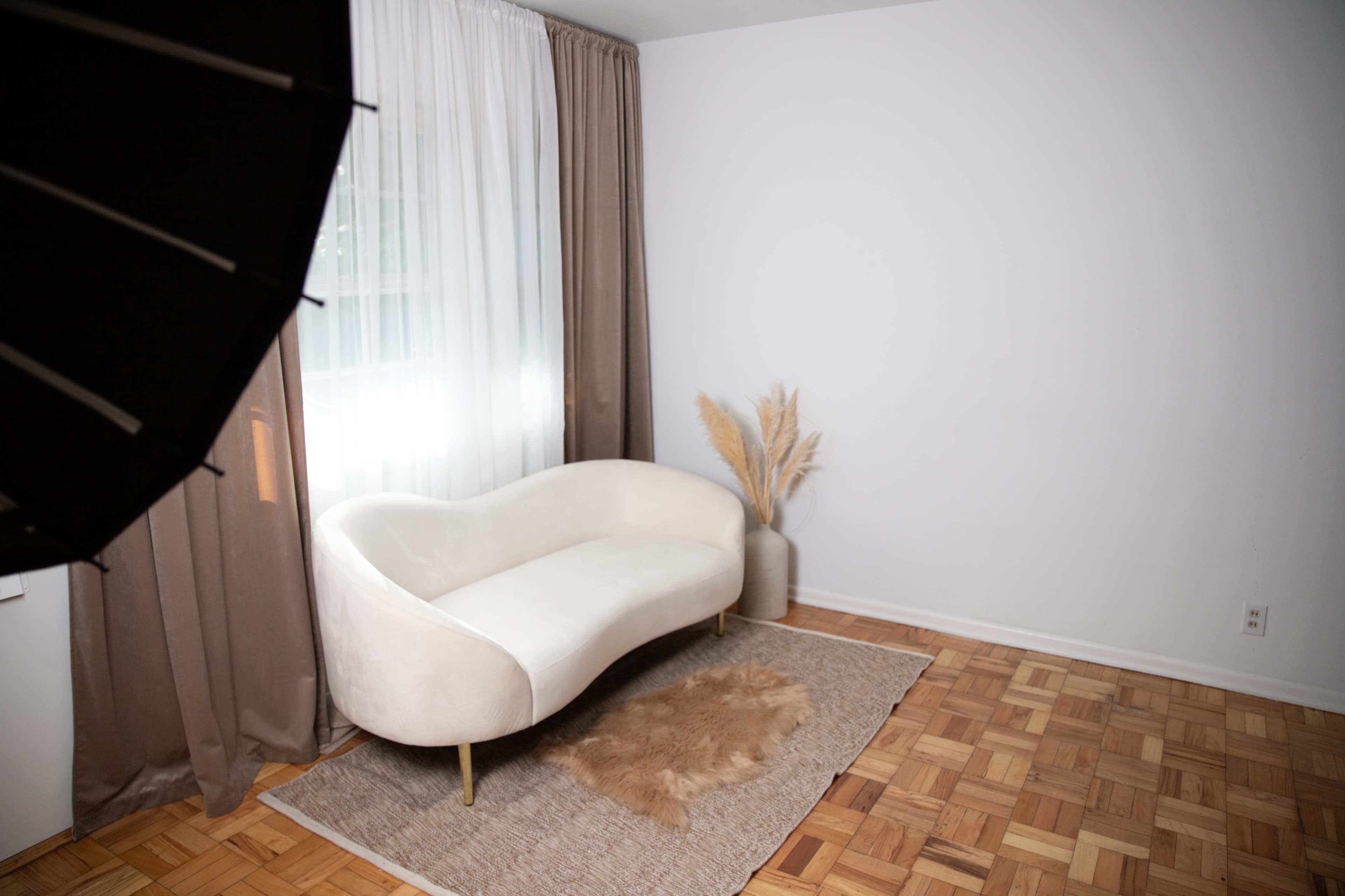 A minimalist interior with a white curved sofa, a textured rug, and decorative plants near a window with sheer curtains.