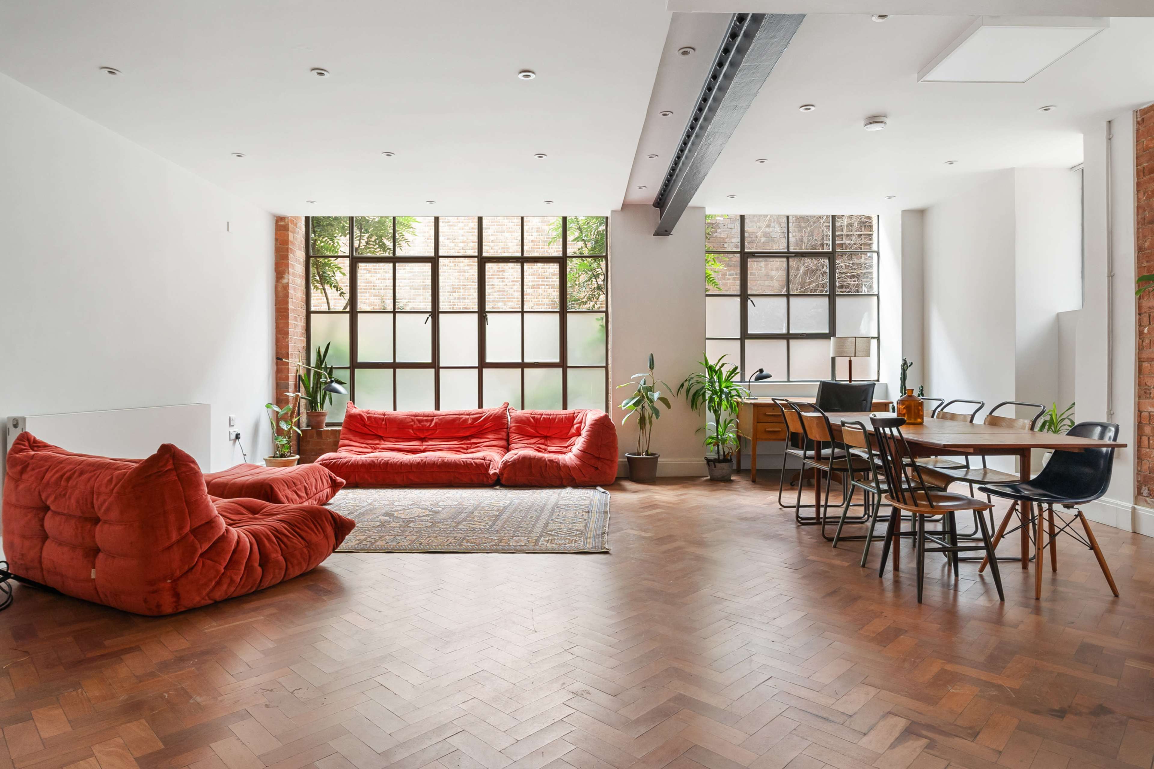 The spacious living area features bright windows, large red beanbag chairs, a wooden dining table, and various indoor plants.