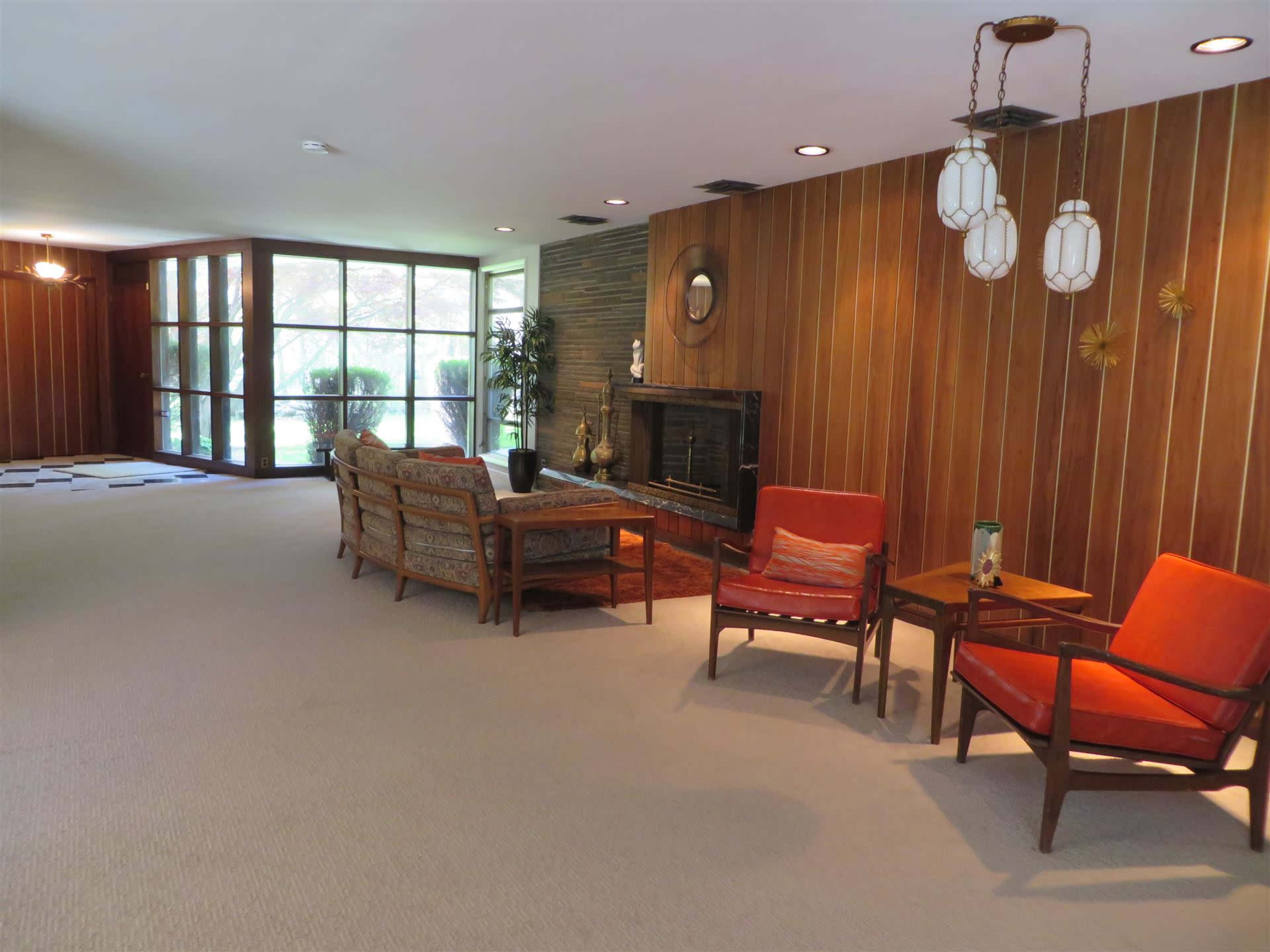 A spacious living area features wooden paneling, a fireplace, and mid-century modern furniture.