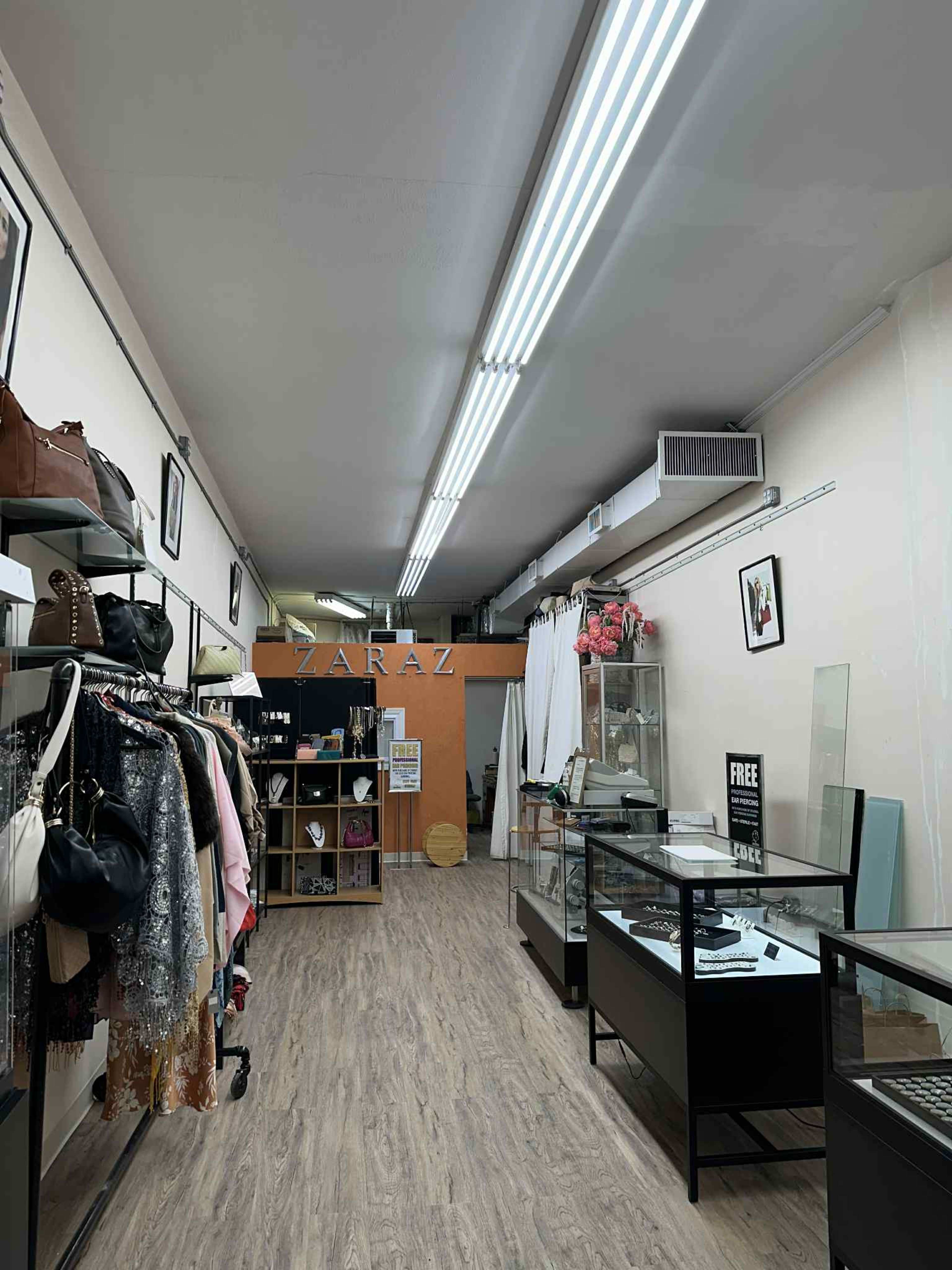 The interior of a retail store features racks of clothing on one side, display cases in the center, and an orange sign with the word "ZARAZ" on the back wall.