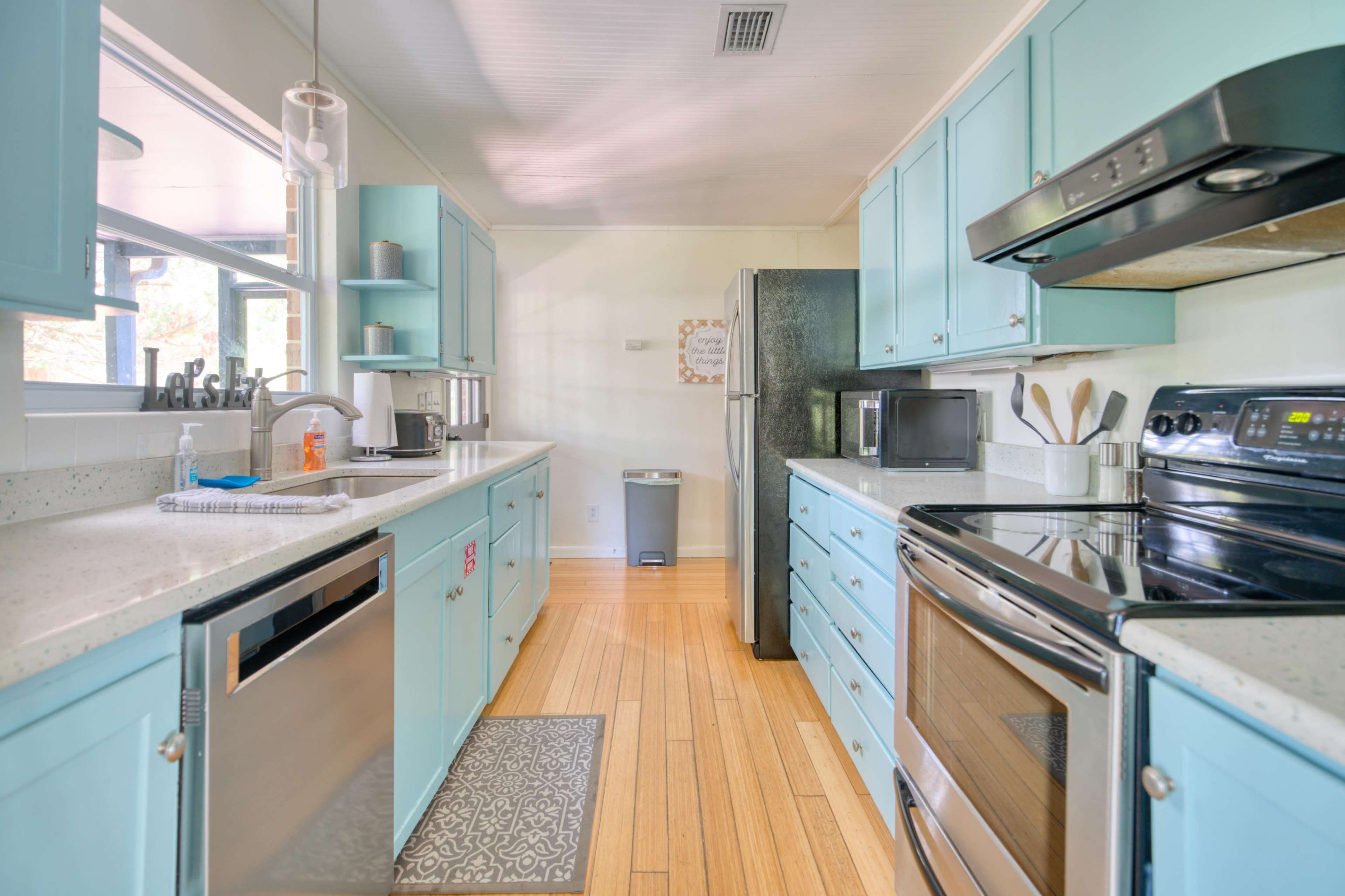 The kitchen features light blue cabinetry, stainless steel appliances, and a clean countertop layout with wooden flooring.