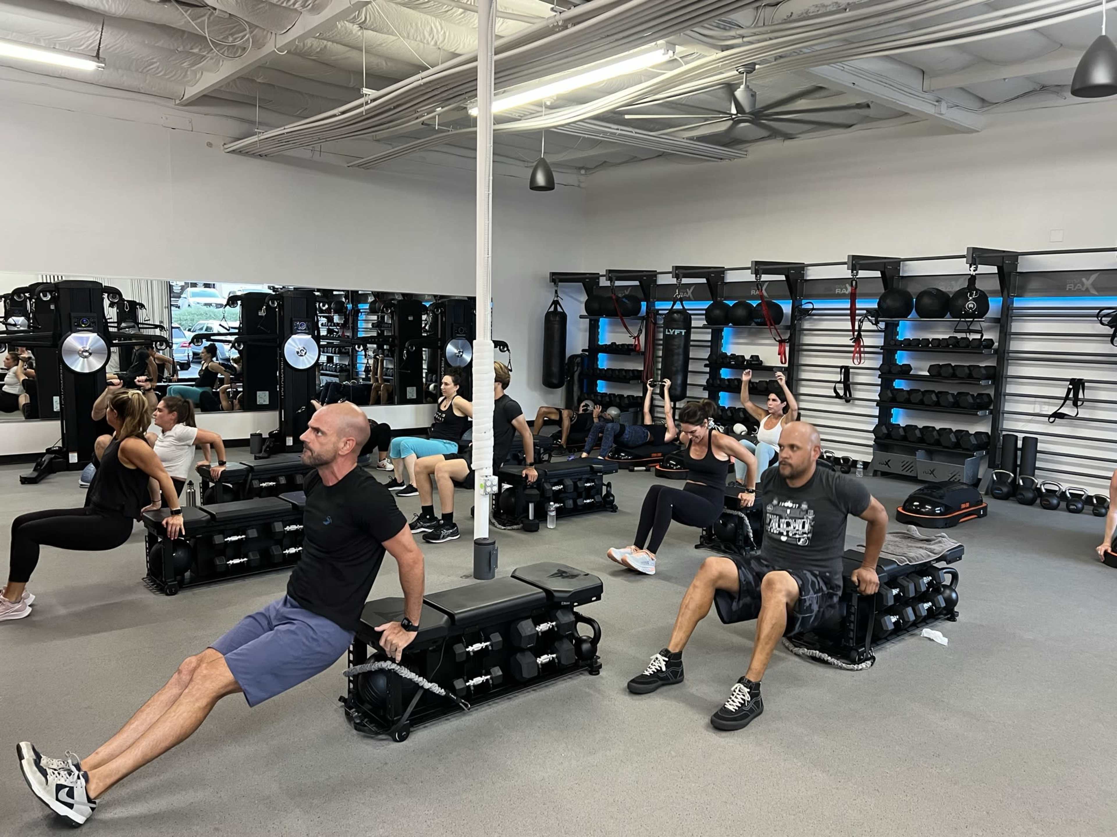 A group of people is engaging in a strength training workout in a gym, using benches and various fitness equipment.
