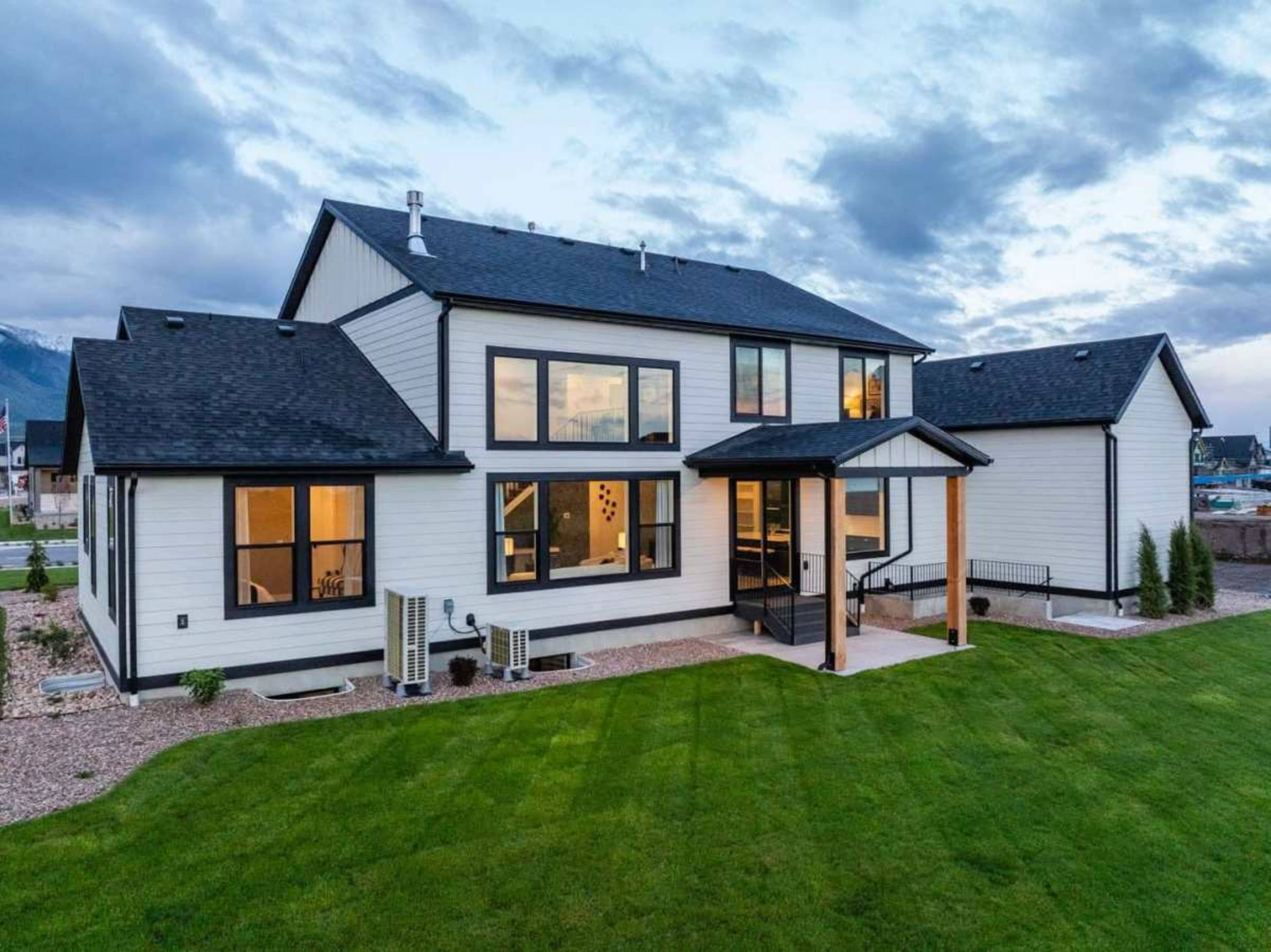 The image shows a modern two-story house with large windows and a neatly maintained lawn surrounded by mountains in the background.