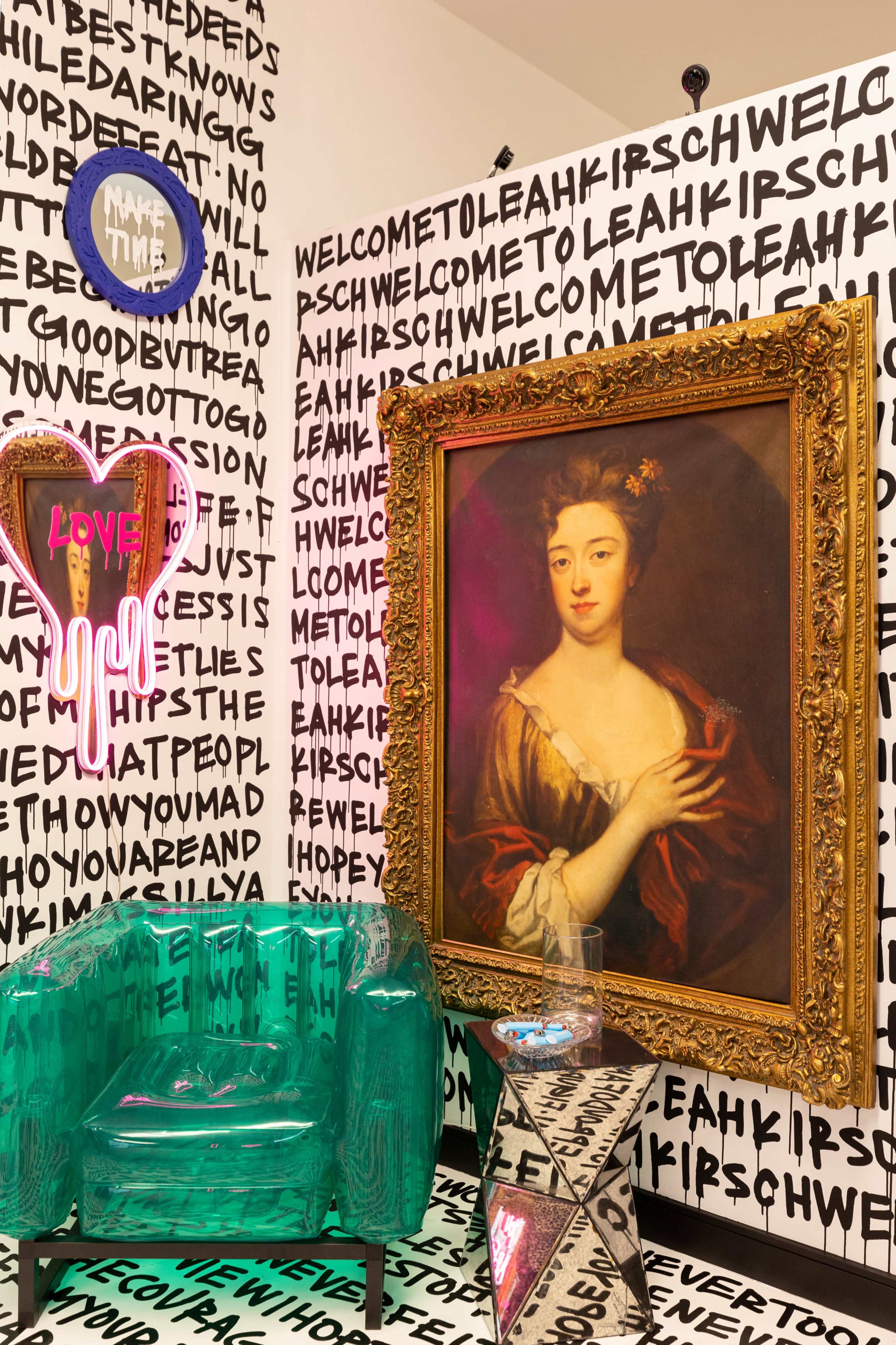 A vibrant room with a large, ornate framed portrait of a woman, surrounded by black and white text patterns on the walls and a transparent green chair.
