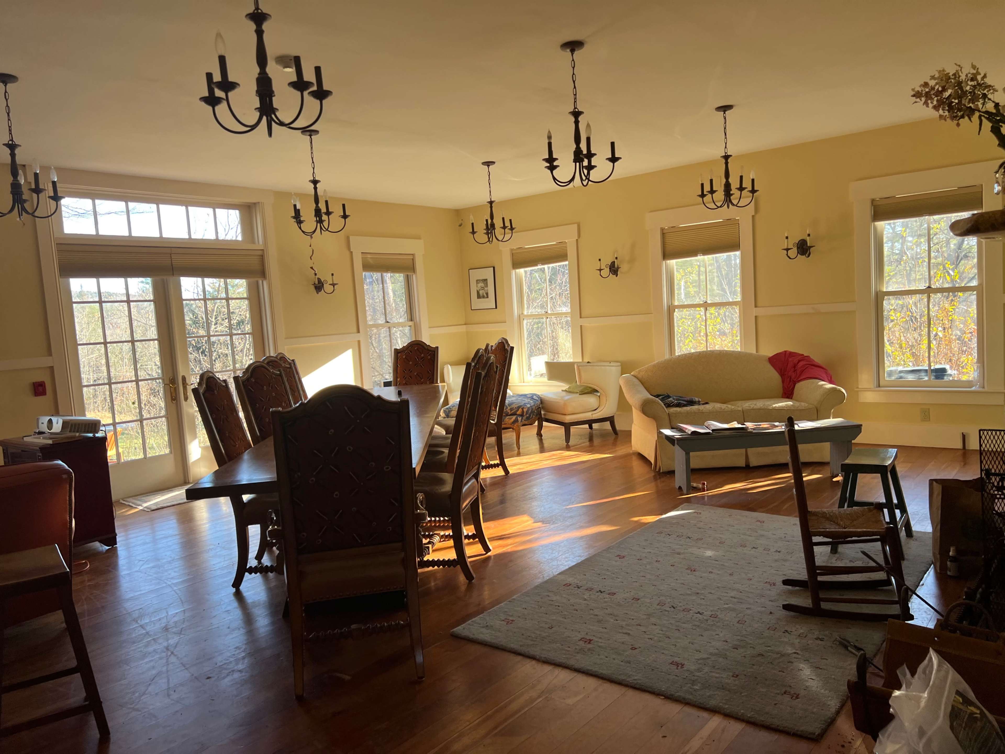 The room features a dining table, several chairs, a couch, and large windows allowing natural light to fill the space.