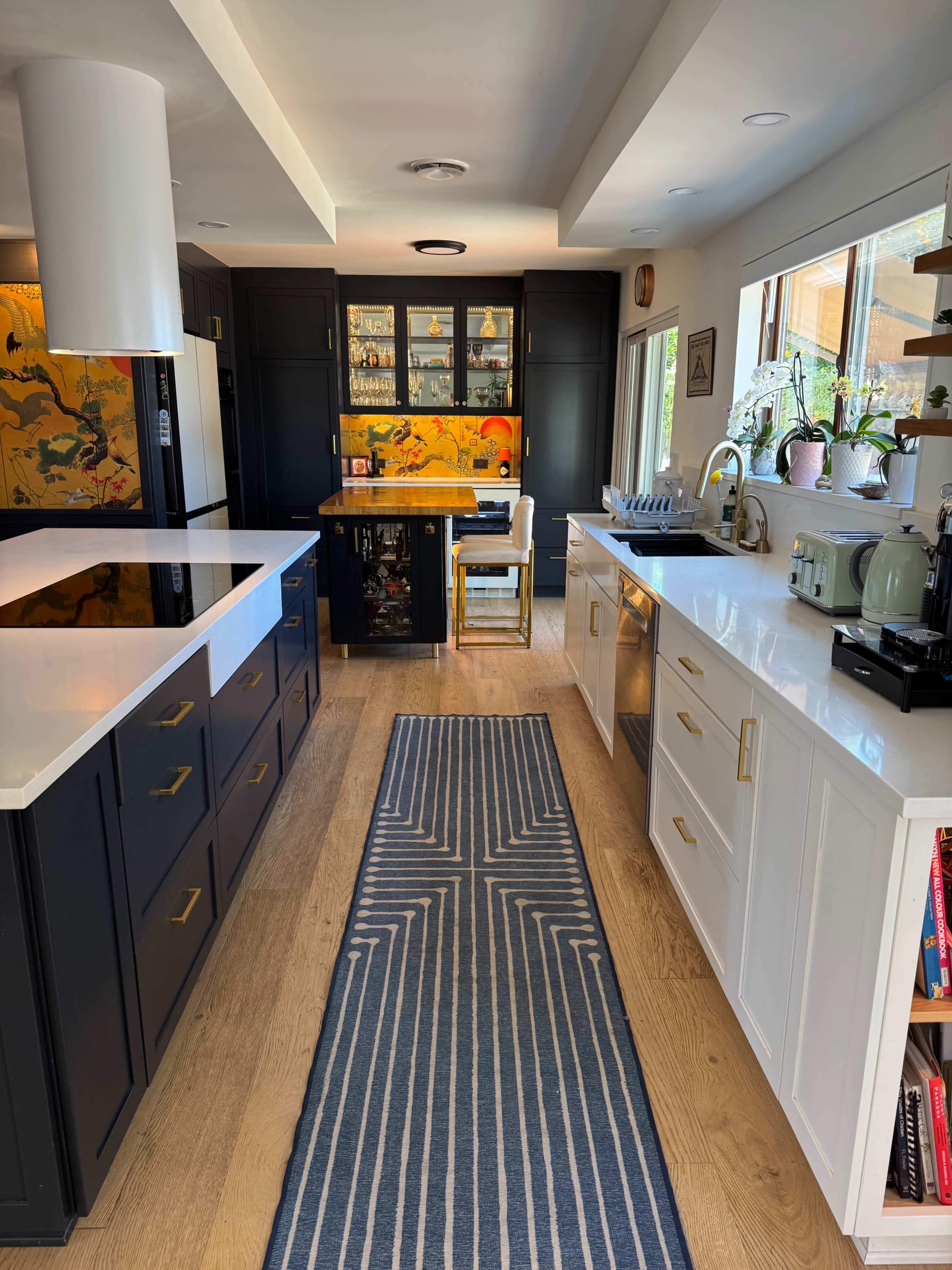 The image shows a modern kitchen featuring white and black cabinetry, a central island, and a long, patterned rug extending down the floor.