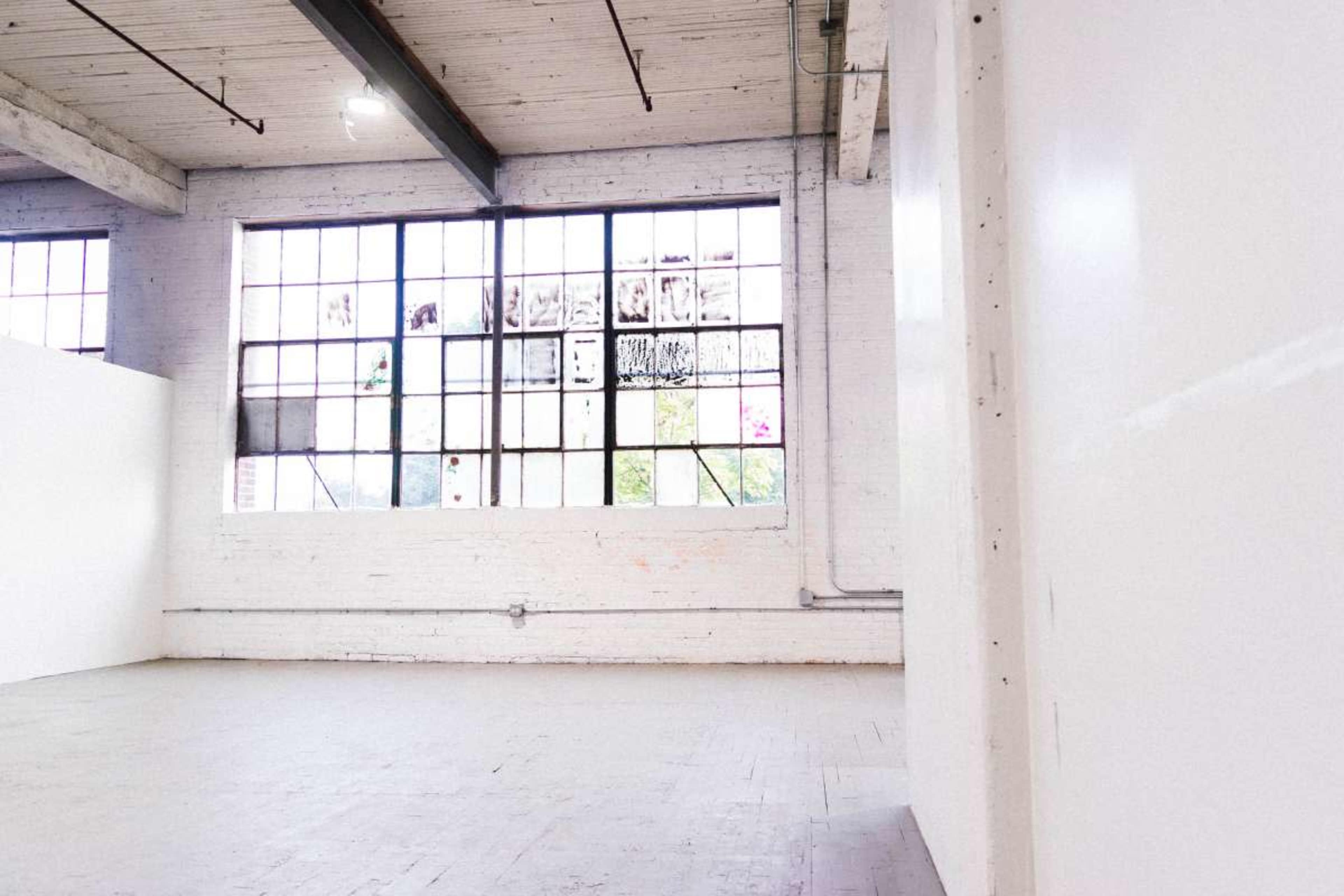 The image shows an empty industrial space with large windows and white walls.