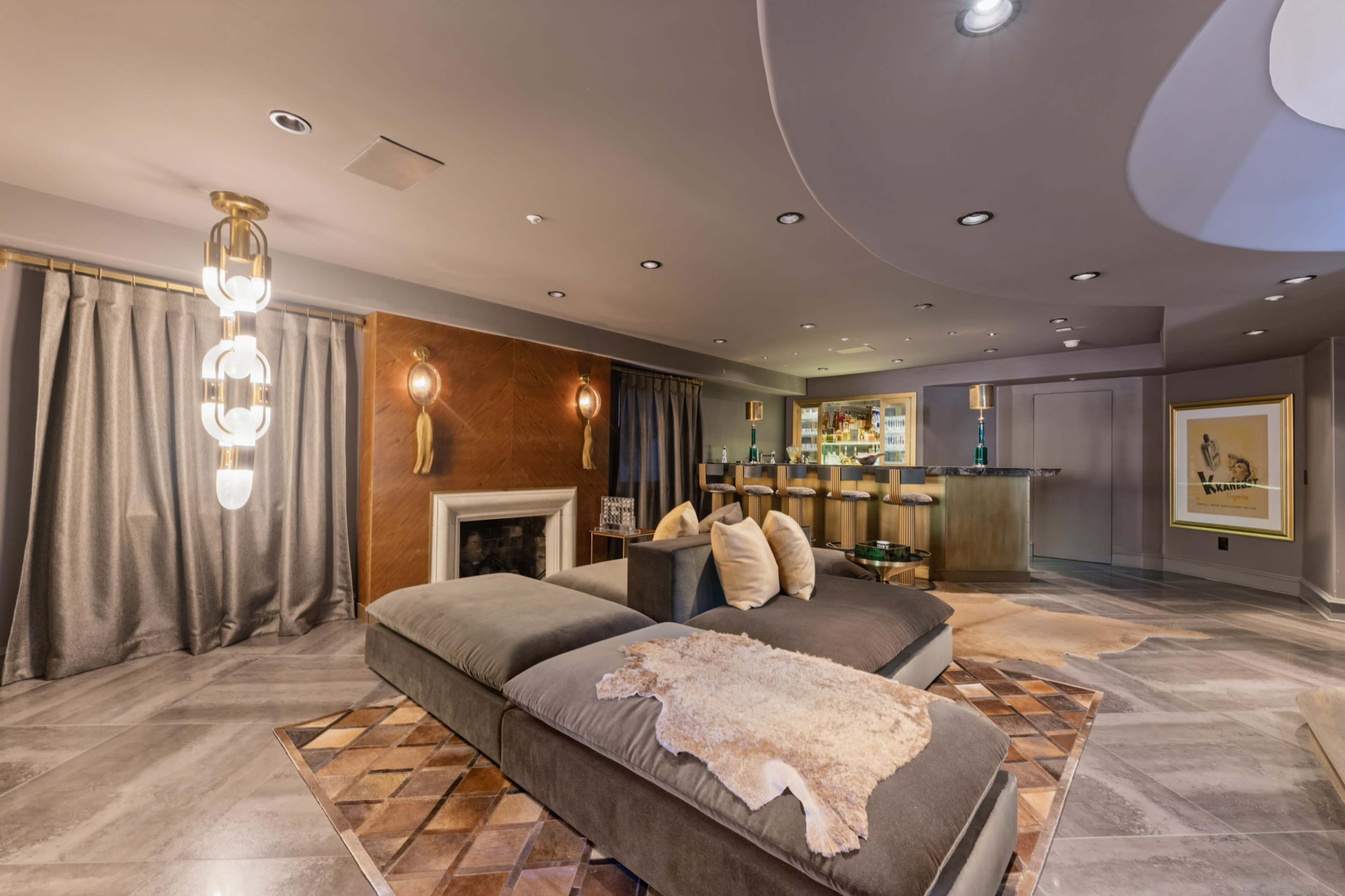 The image shows a modern living room featuring a sectional couch with decorative pillows, a fireplace, and an adjacent bar area with stools.