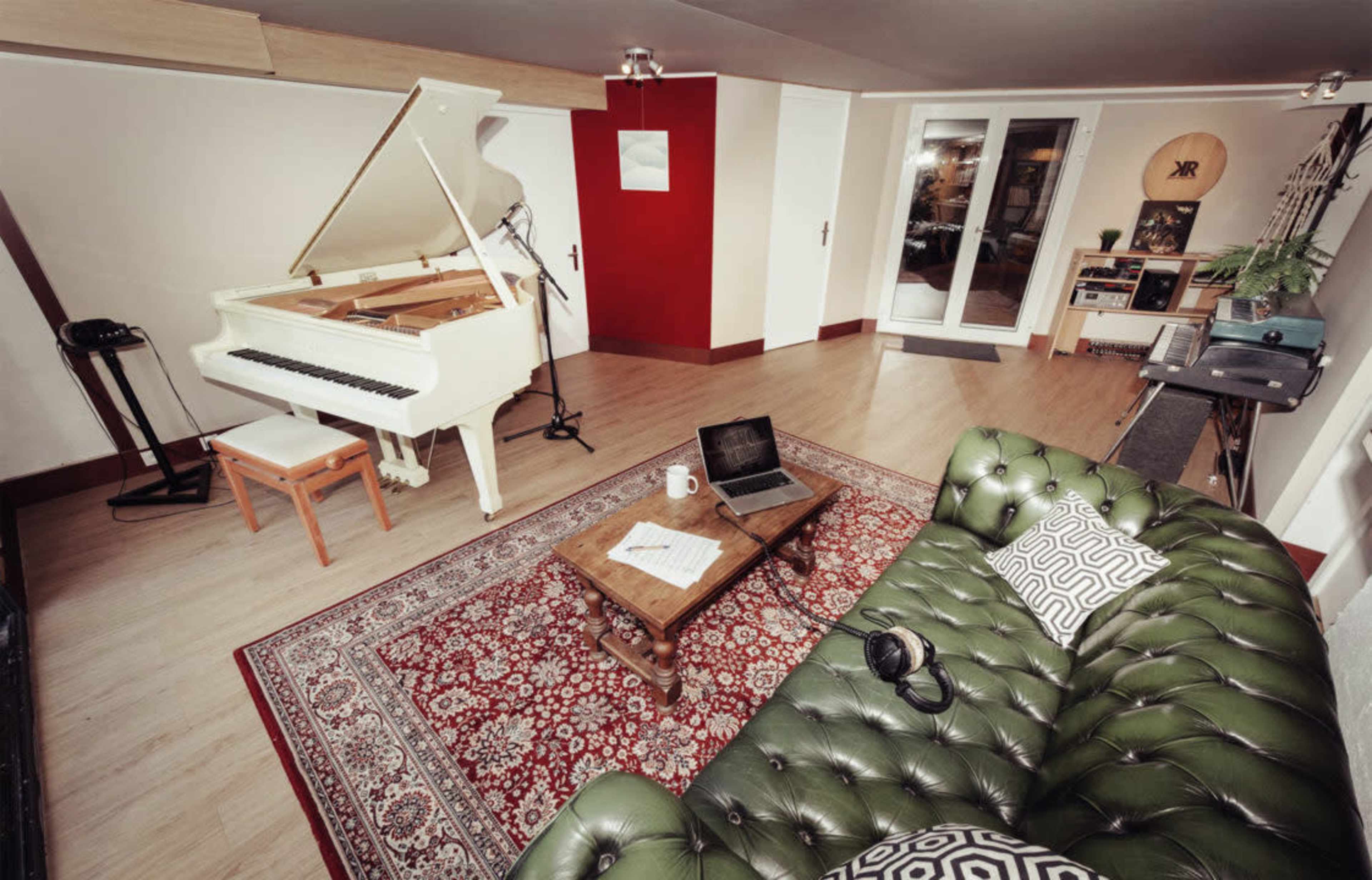 A music room featuring a white grand piano, a green leather sofa, a wooden coffee table, and a laptop on the floor.