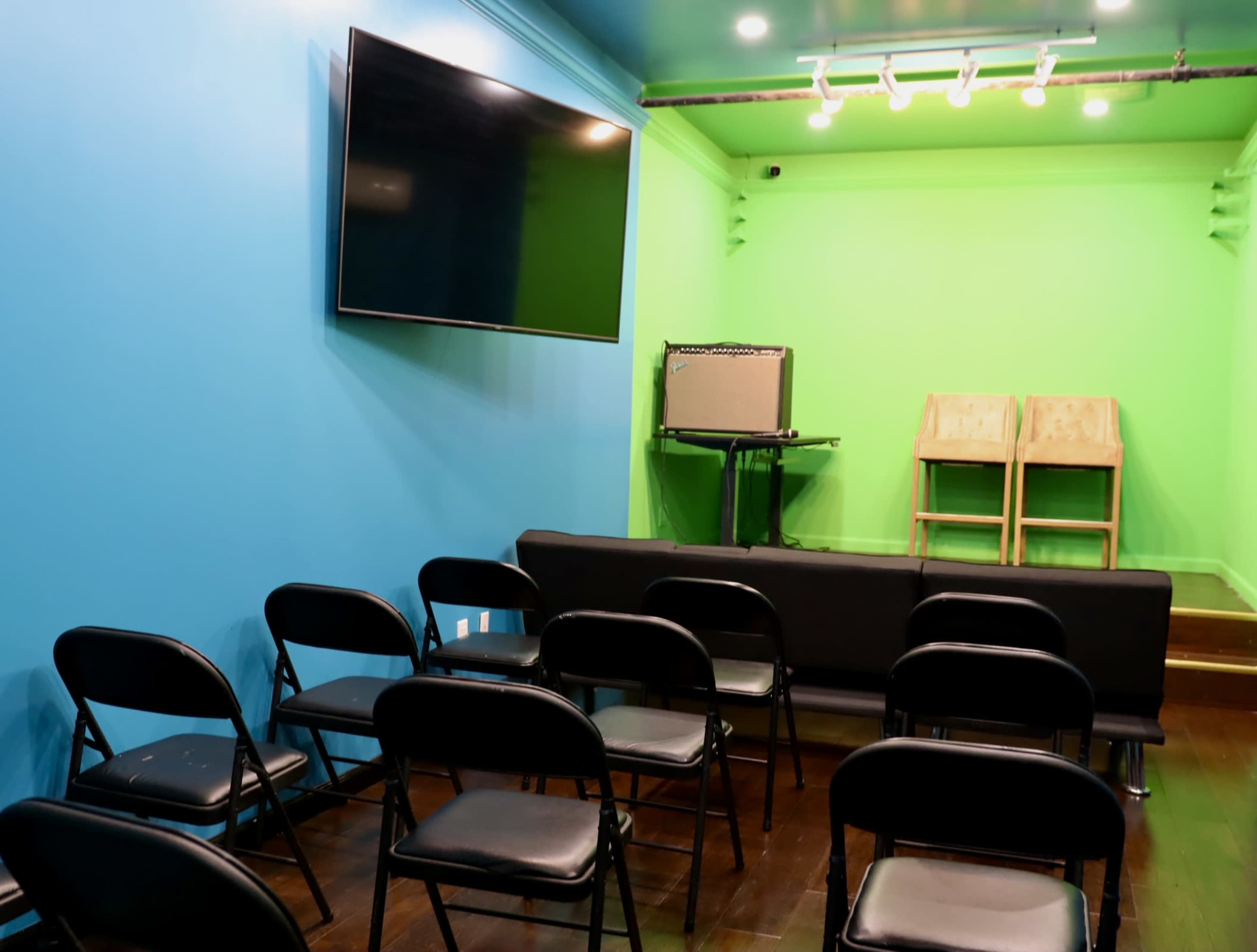 A small room with a blue wall, green background, several black folding chairs arranged in rows, a sofa, and a television mounted on the wall.