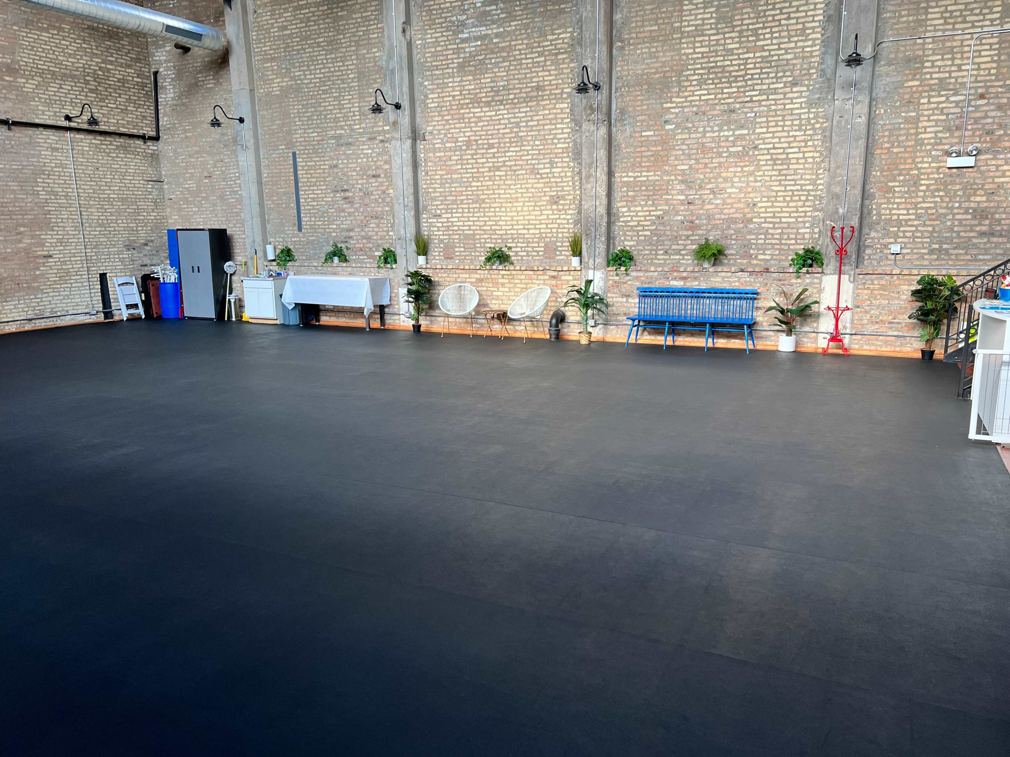 A spacious indoor area with a black floor, brick walls, and potted plants arranged along the sides.
