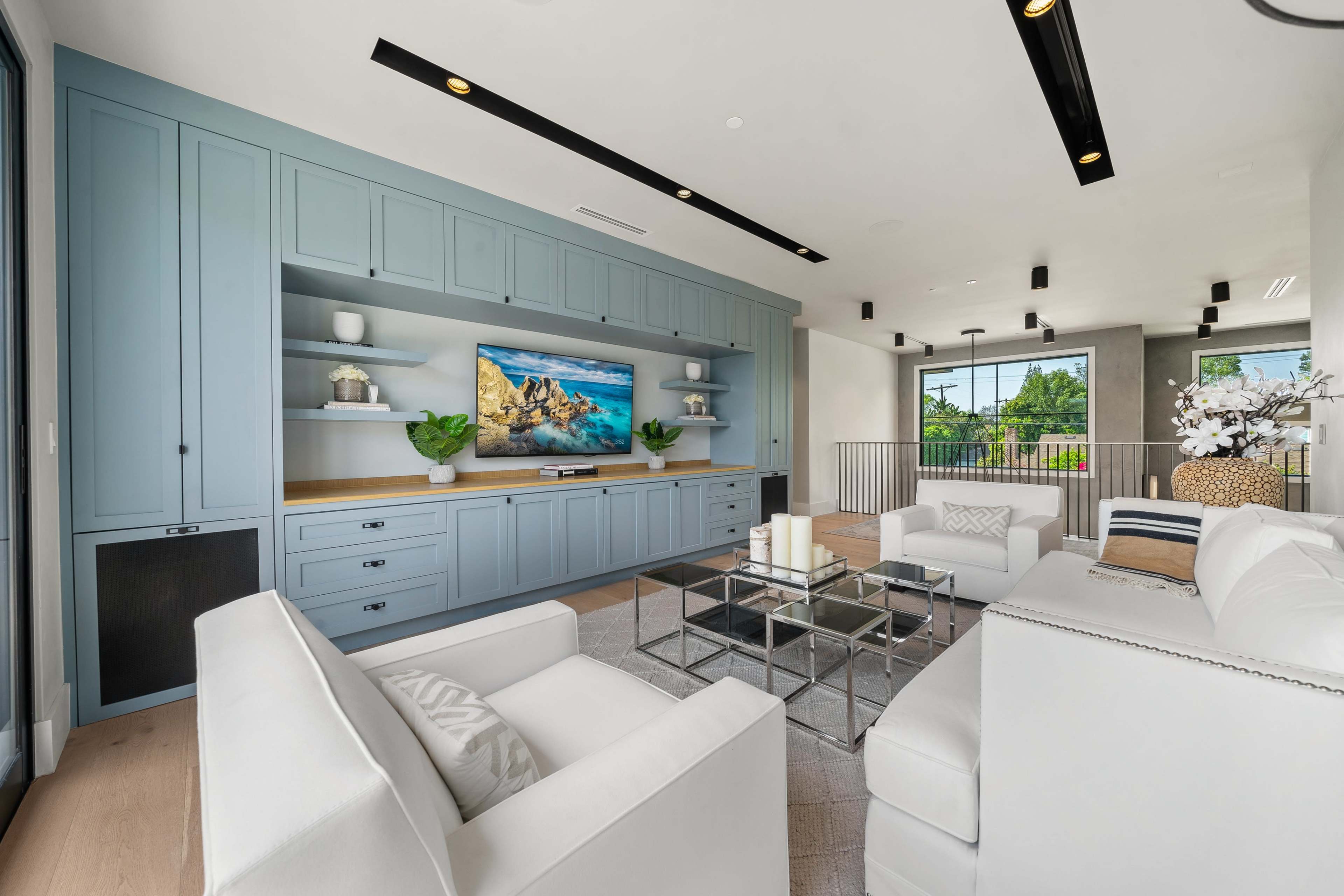 The image shows a modern living room featuring a light blue entertainment center, a large television mounted on the wall, and white furniture set around a glass coffee table.