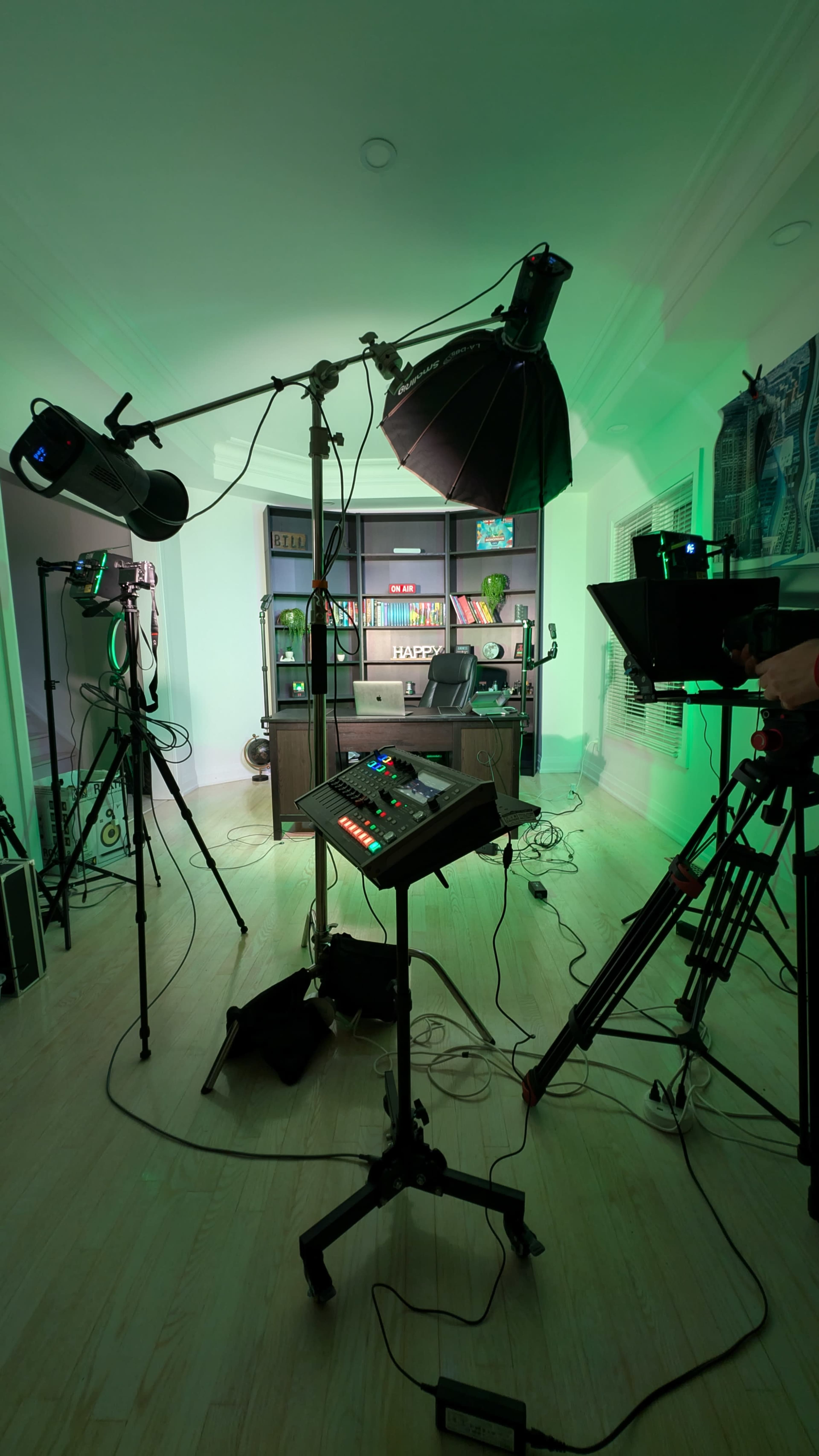 The scene shows a video production setup with multiple cameras, lights, and a control panel placed in a room decorated with shelves.