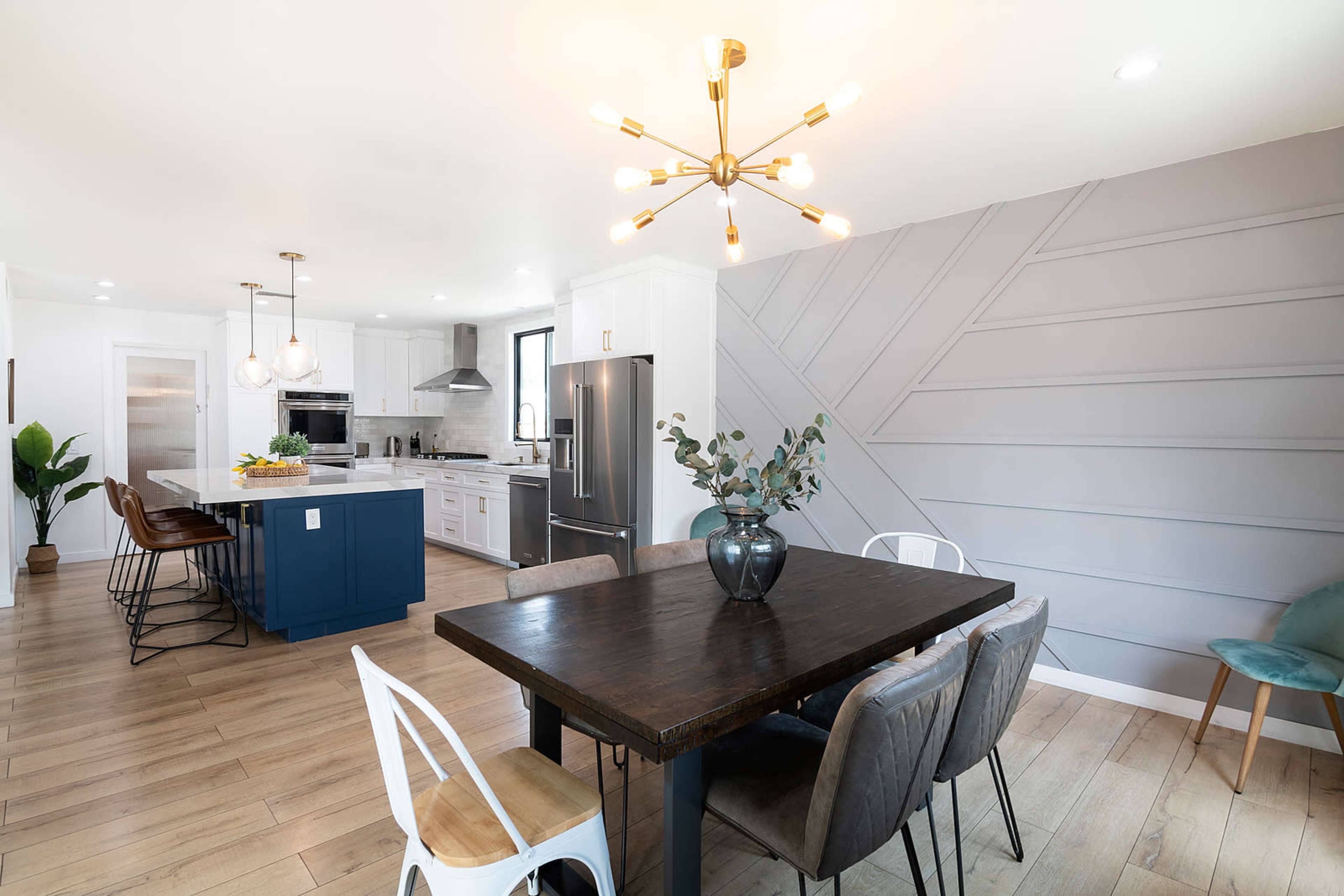 A contemporary kitchen features a large dining table, modern lighting fixtures, and a mix of cabinetry and appliances.