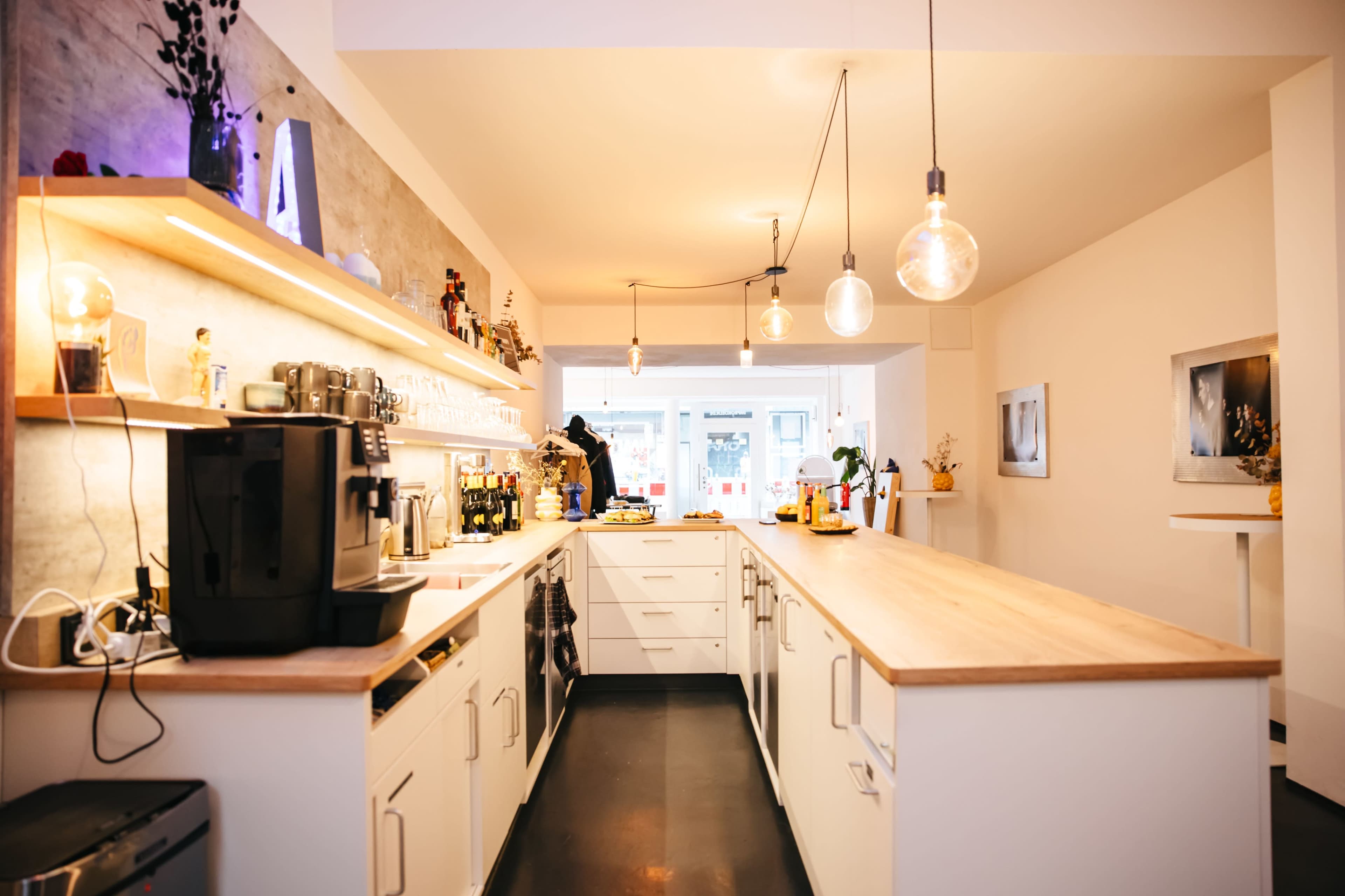 A modern kitchen features a long wooden counter, white cabinets, and pendant lights overhead.
