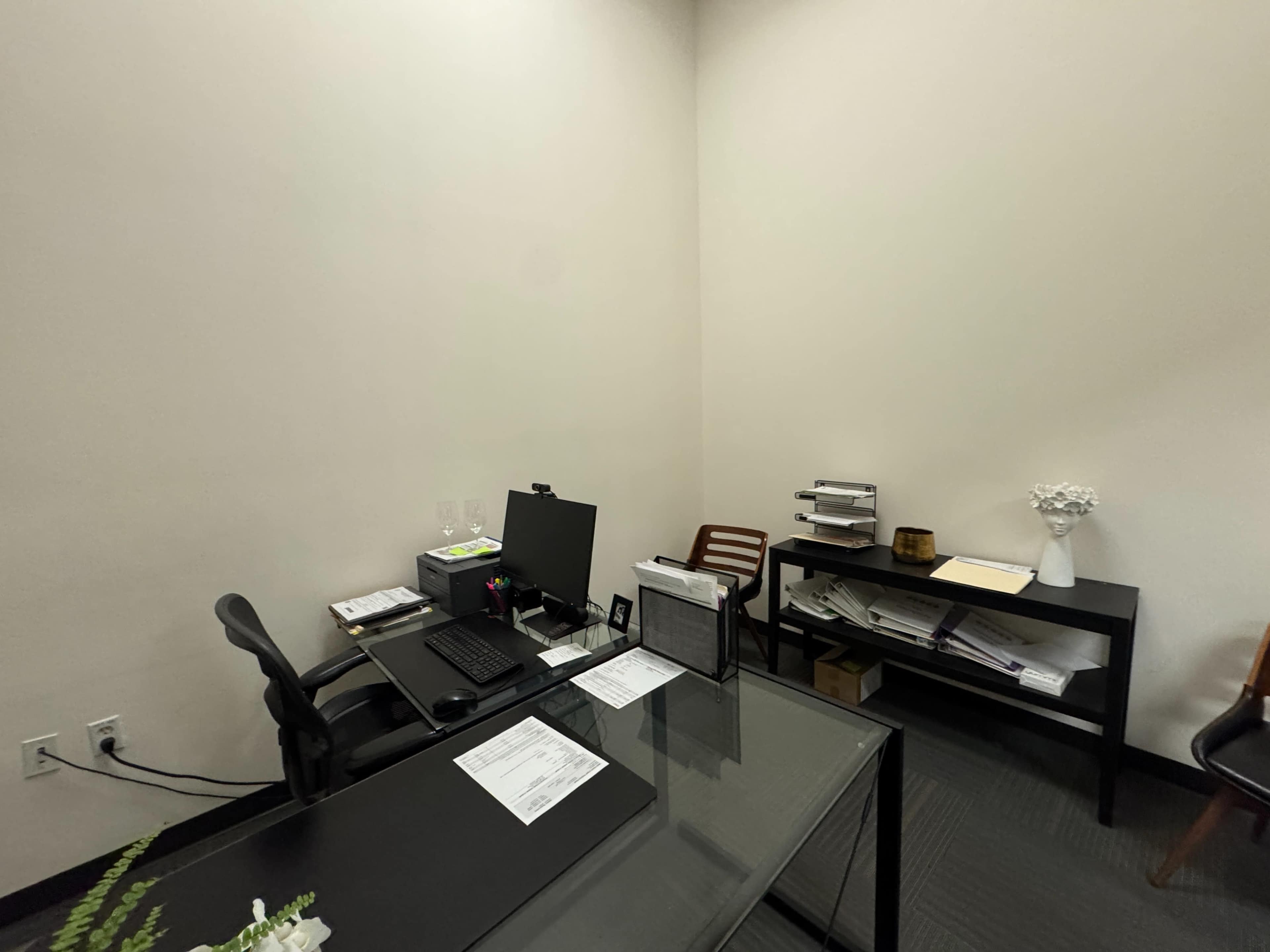 The image shows a small office space with a desk, computer, chair, and shelves containing various documents.