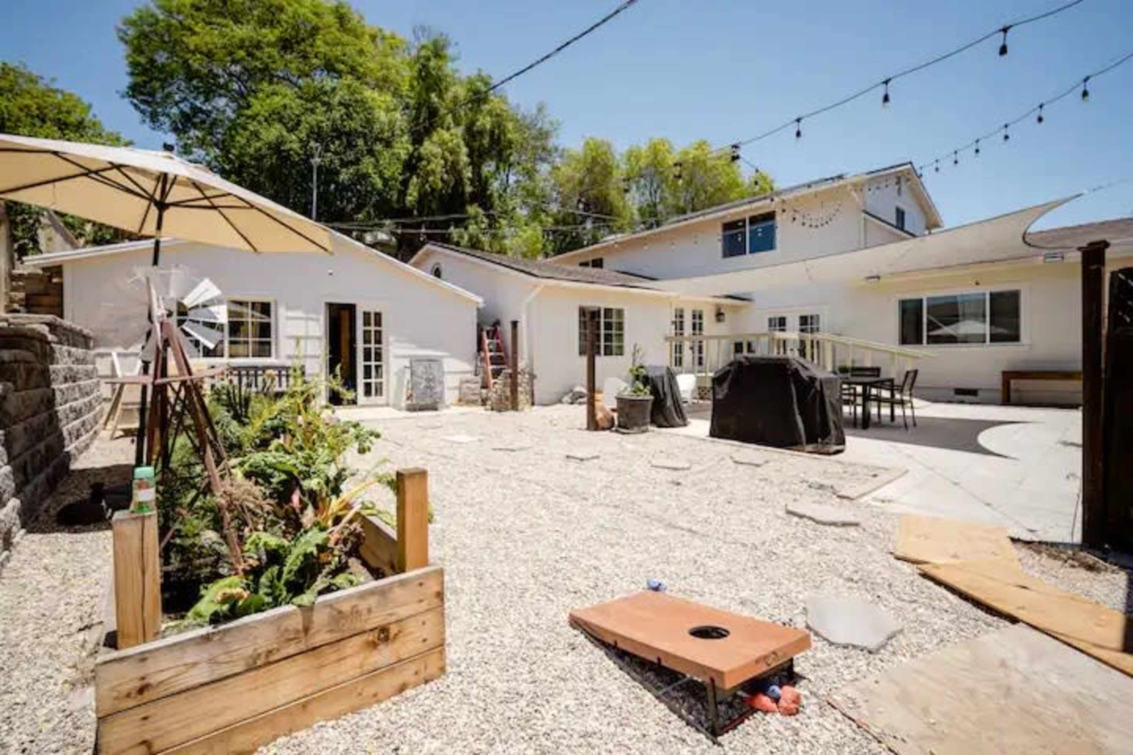 A backyard area with a gravel landscape, a barbecue grill, garden boxes, and string lights overhead.